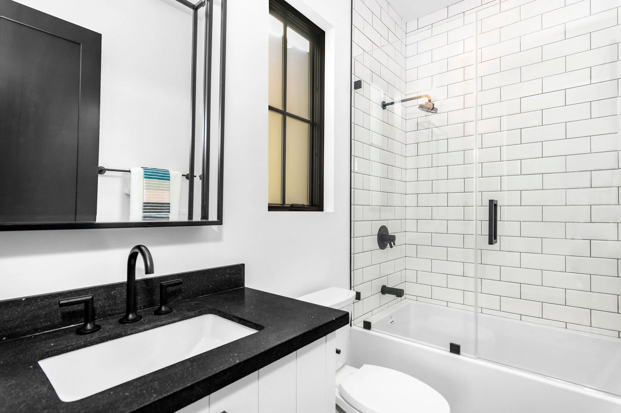 Modern bathroom with black countertop and fixtures, white subway tile shower, and a towel on a rack.