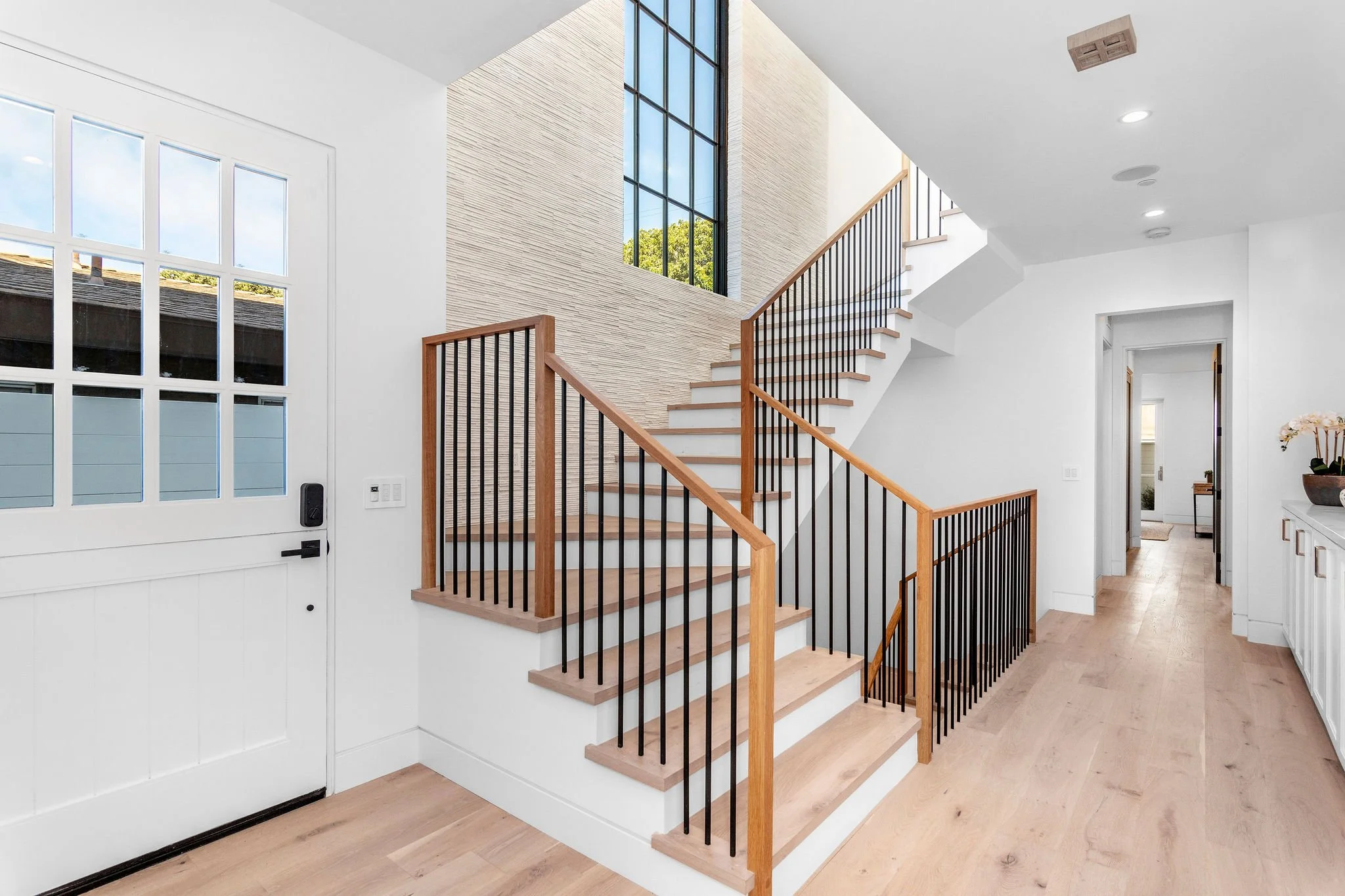Contemporary home interior with wooden staircase, white walls, large window, and wooden flooring.