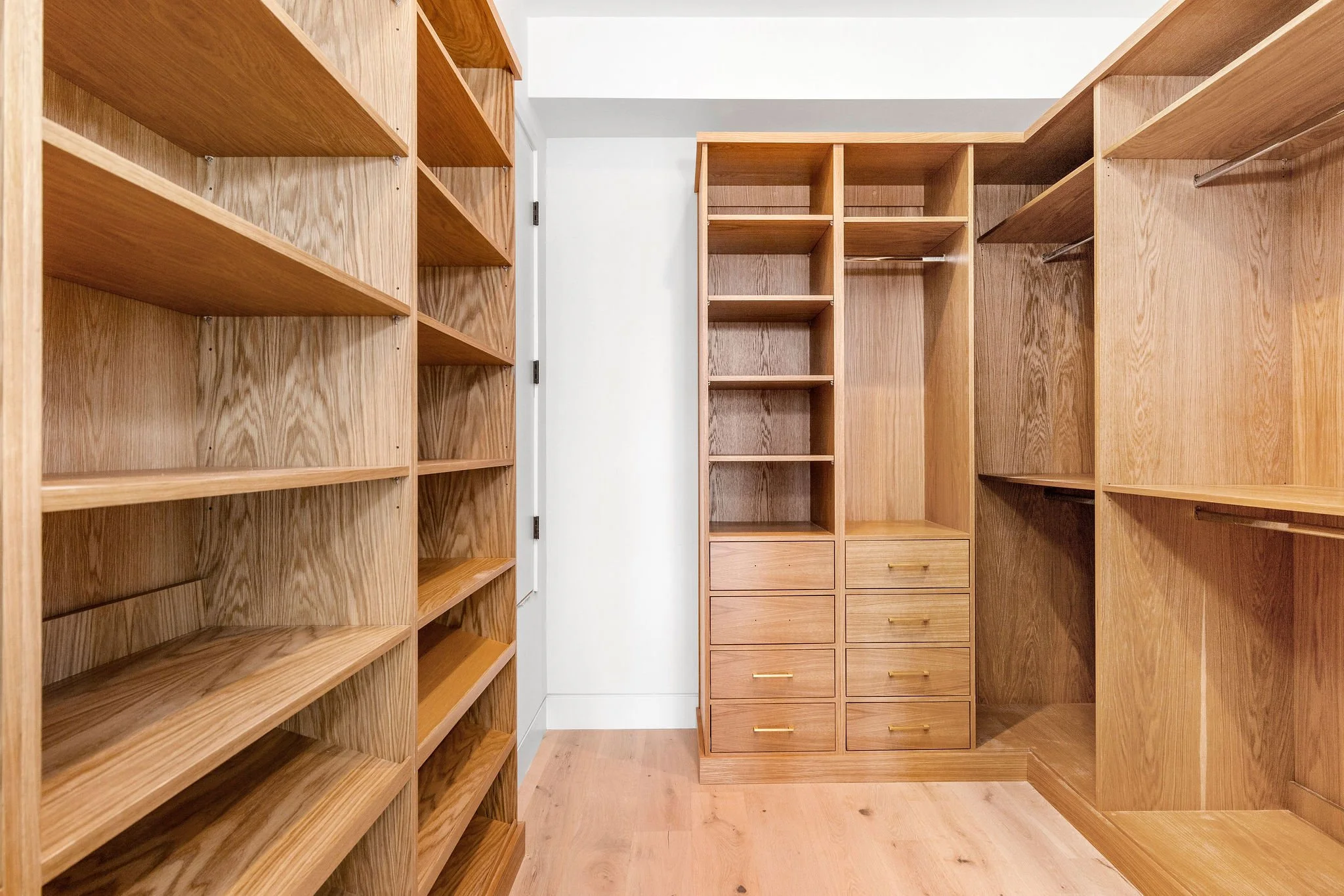Walk-in closet with wooden shelves, drawers, and hanging racks.