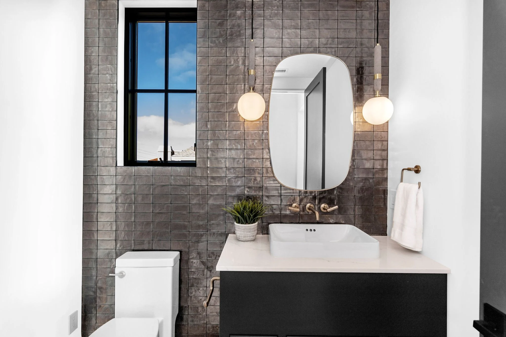 Modern bathroom with window, mirror, sink, toilet, and towel rack.