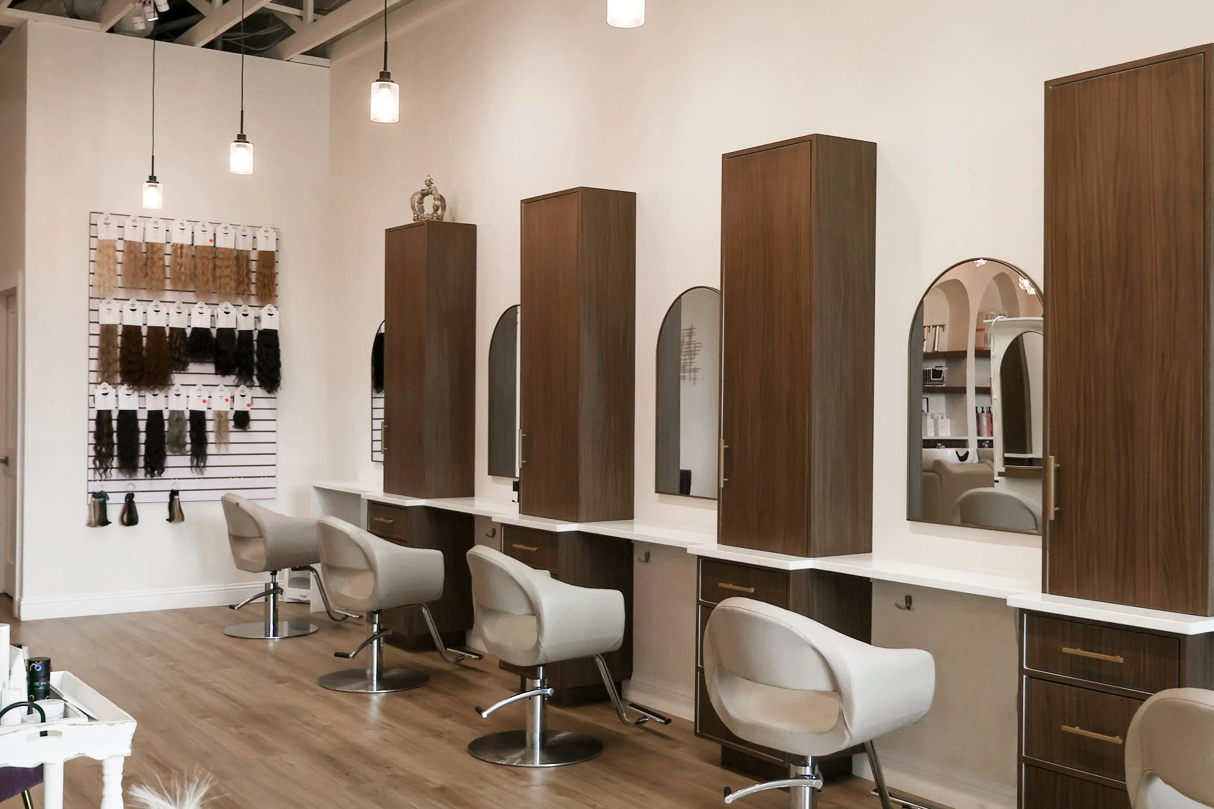 Salon with white chairs, wooden cabinets, mirrors, and hair color display on the wall.