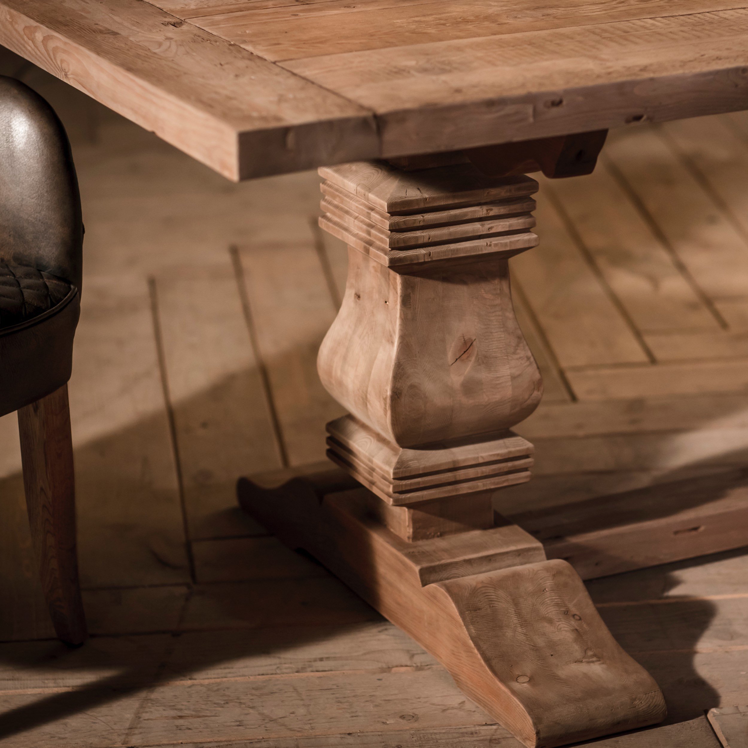 Detalle de una mesa de madera maciza con base tallada y una silla de respaldo de cuero negro.