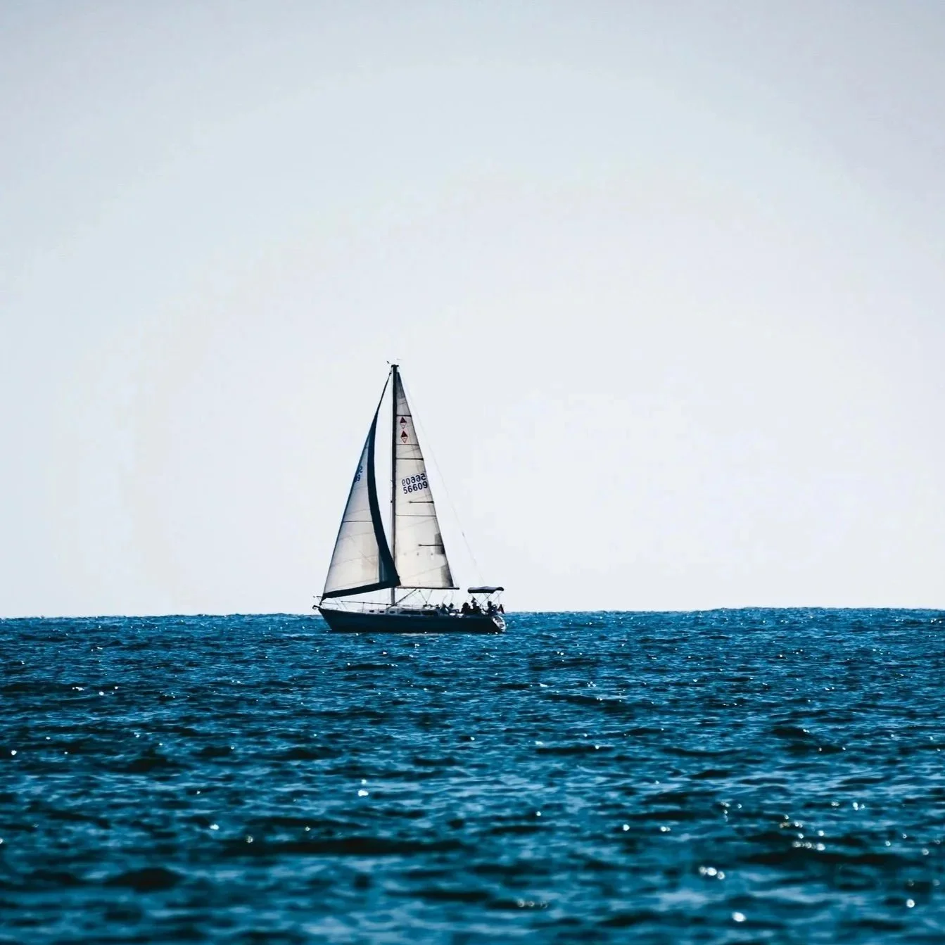 A sailboat with white sails on the open ocean during daytime.