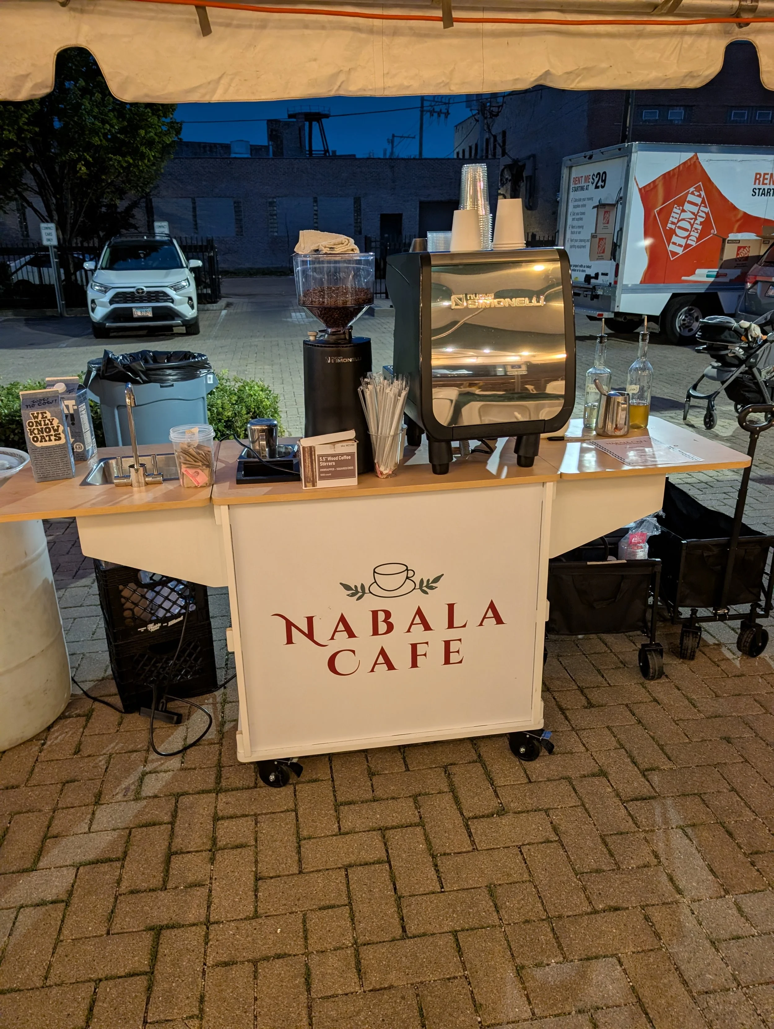 Nabala Cafe outdoor coffee cart with espresso machine, coffee grinder, cups, and coffee beans under a canopy