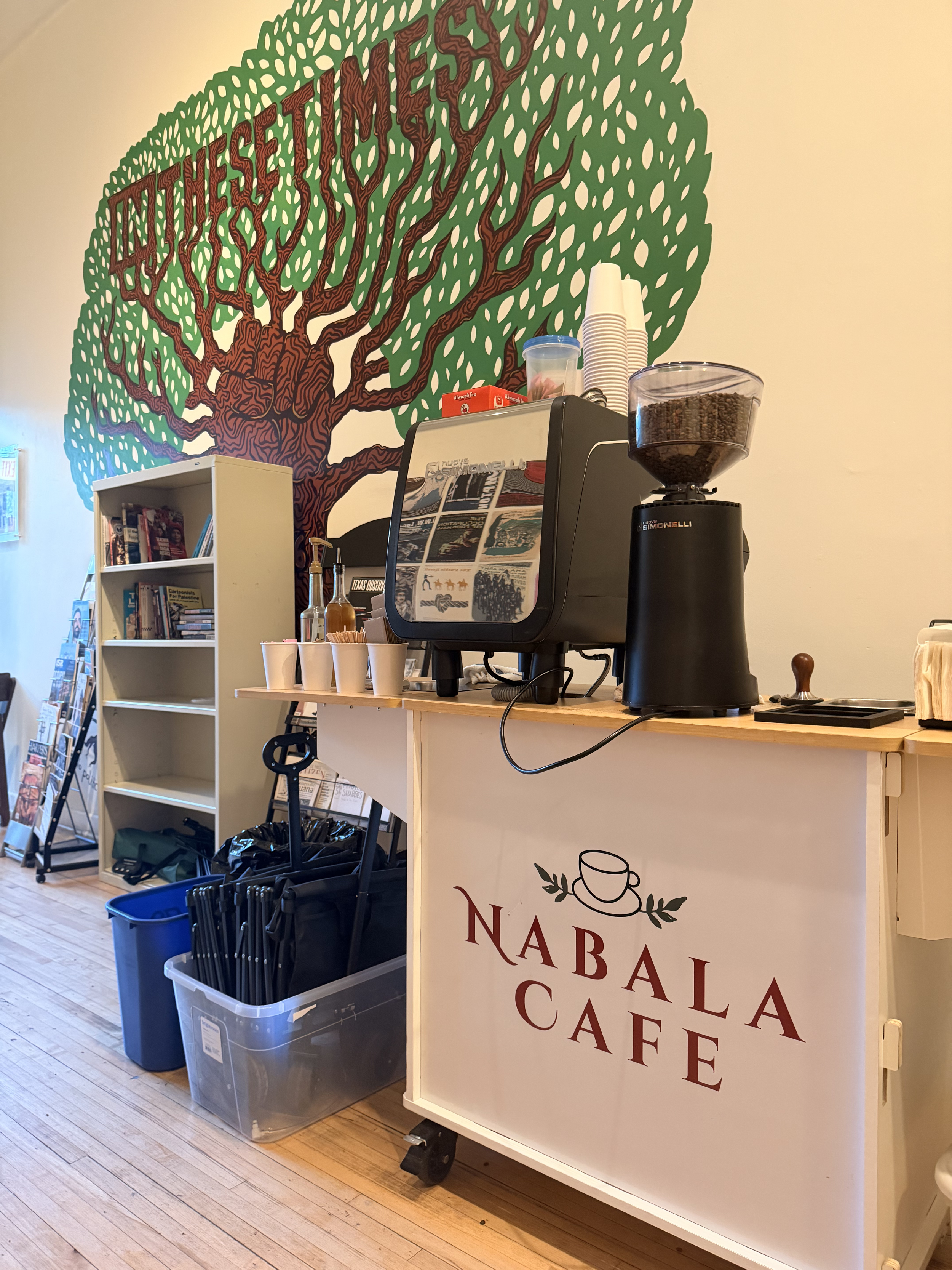 Nabala Cafe coffee bar with espresso machine, coffee grinder, paper cups, and colorful tree mural