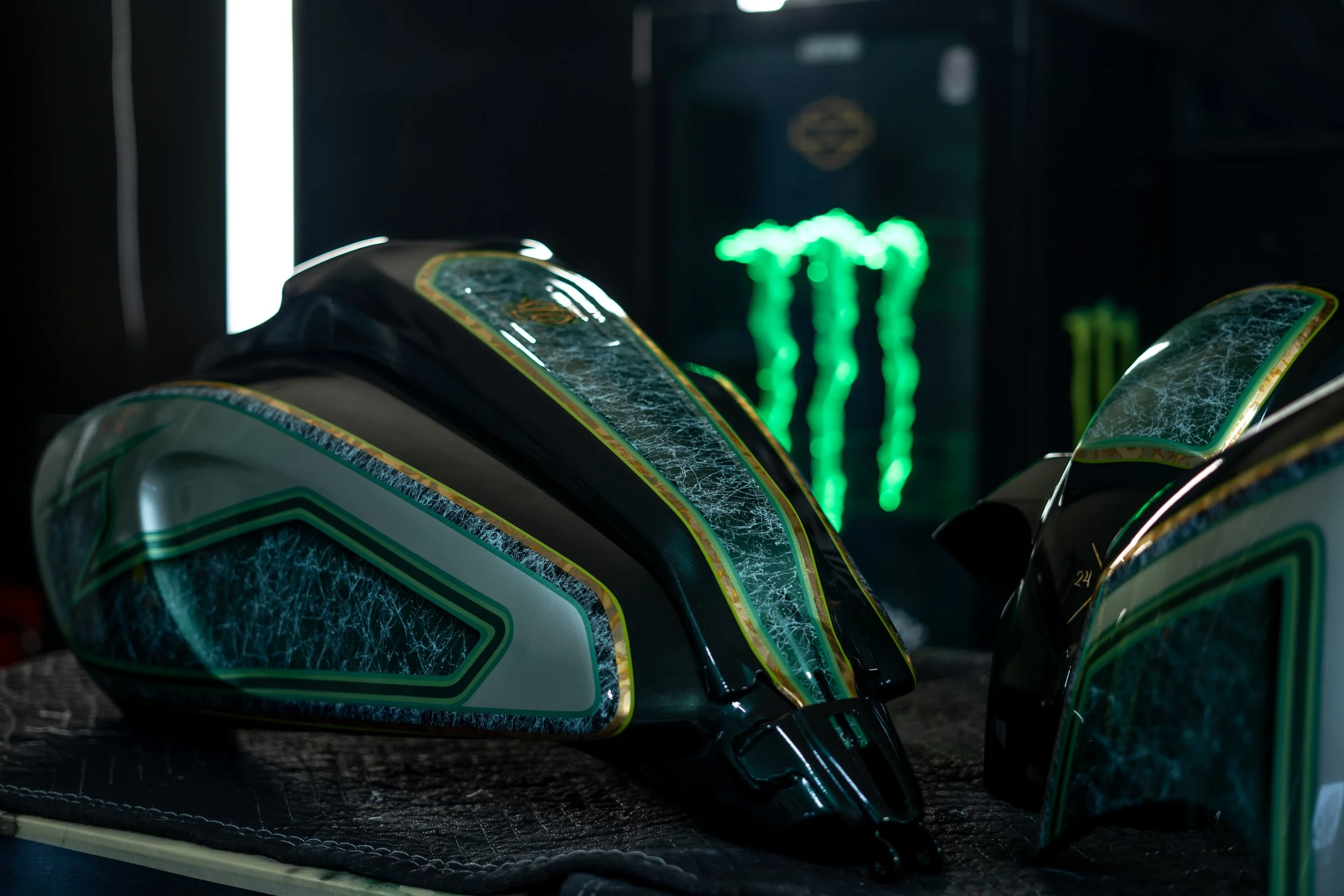 Motorcycle helmets with green and black designs on a textured surface, with a neon green Monster Energy logo in the background.