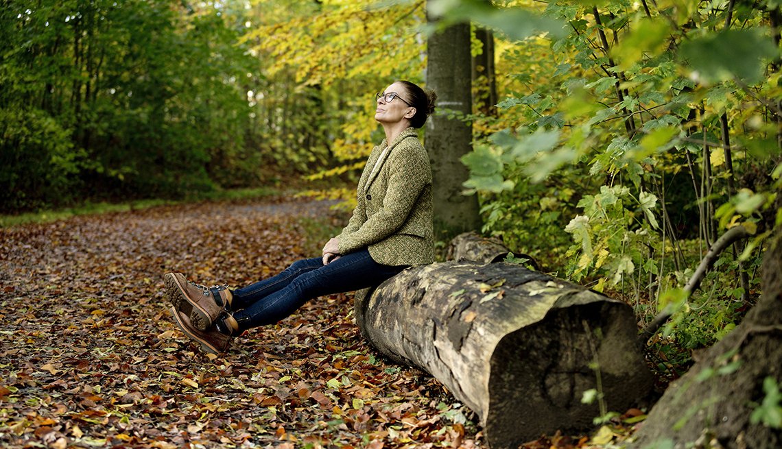 Woman sitting on a log in a forest reflecting quietly, representing overcoming feeling behind in life and reconnecting with purpose