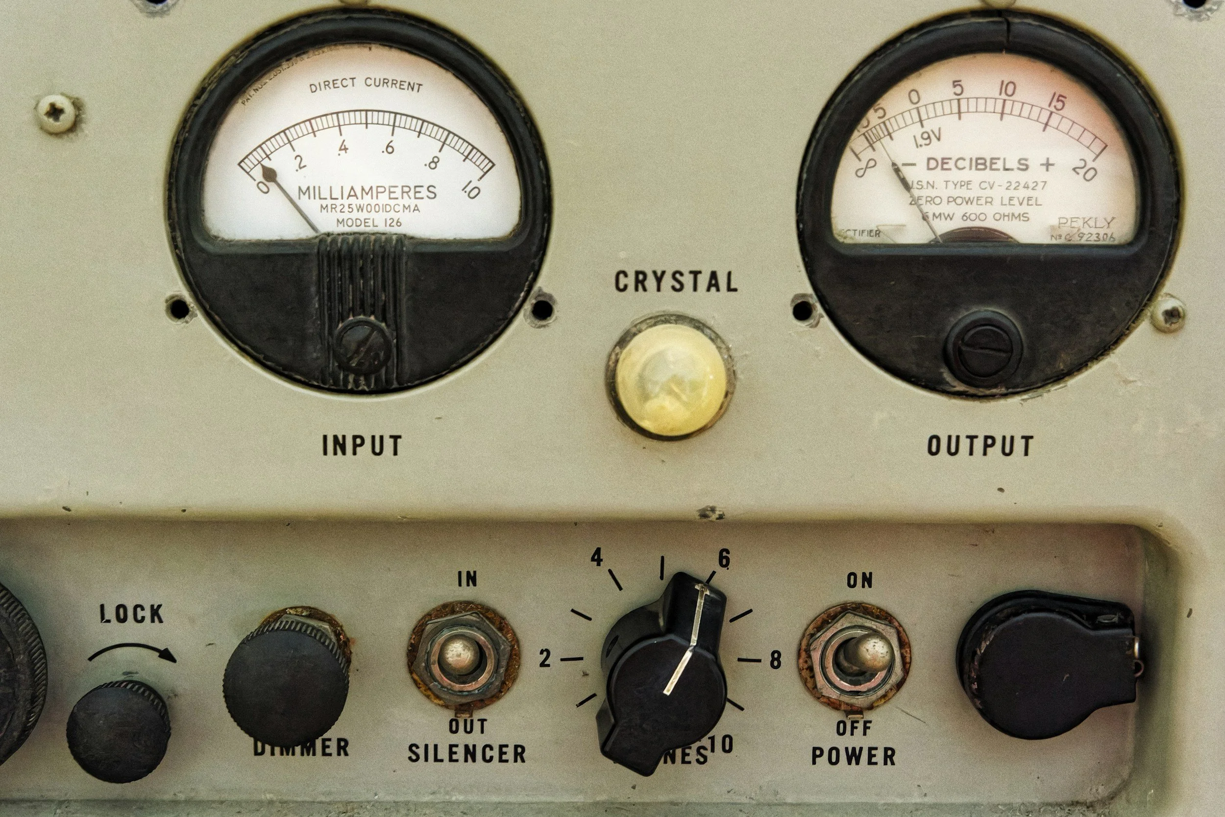 A vintage electronic device with two gauges labeled 'Input' and 'Output,' a yellow button labeled 'Crystal,' and various knobs and switches for power, dimmer, and silencer adjustments.