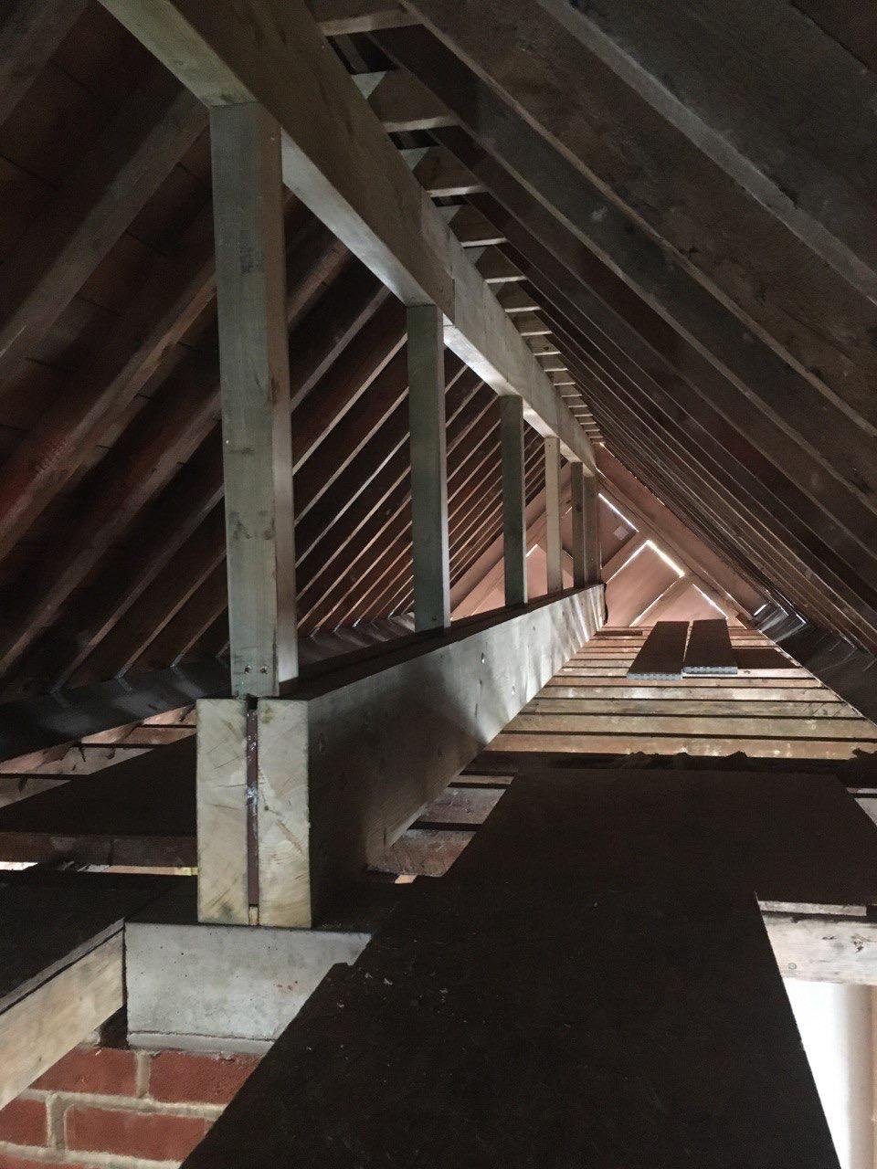 Looking up into an attic or roof space showing wooden rafters, beams, and a makeshift wooden railing.