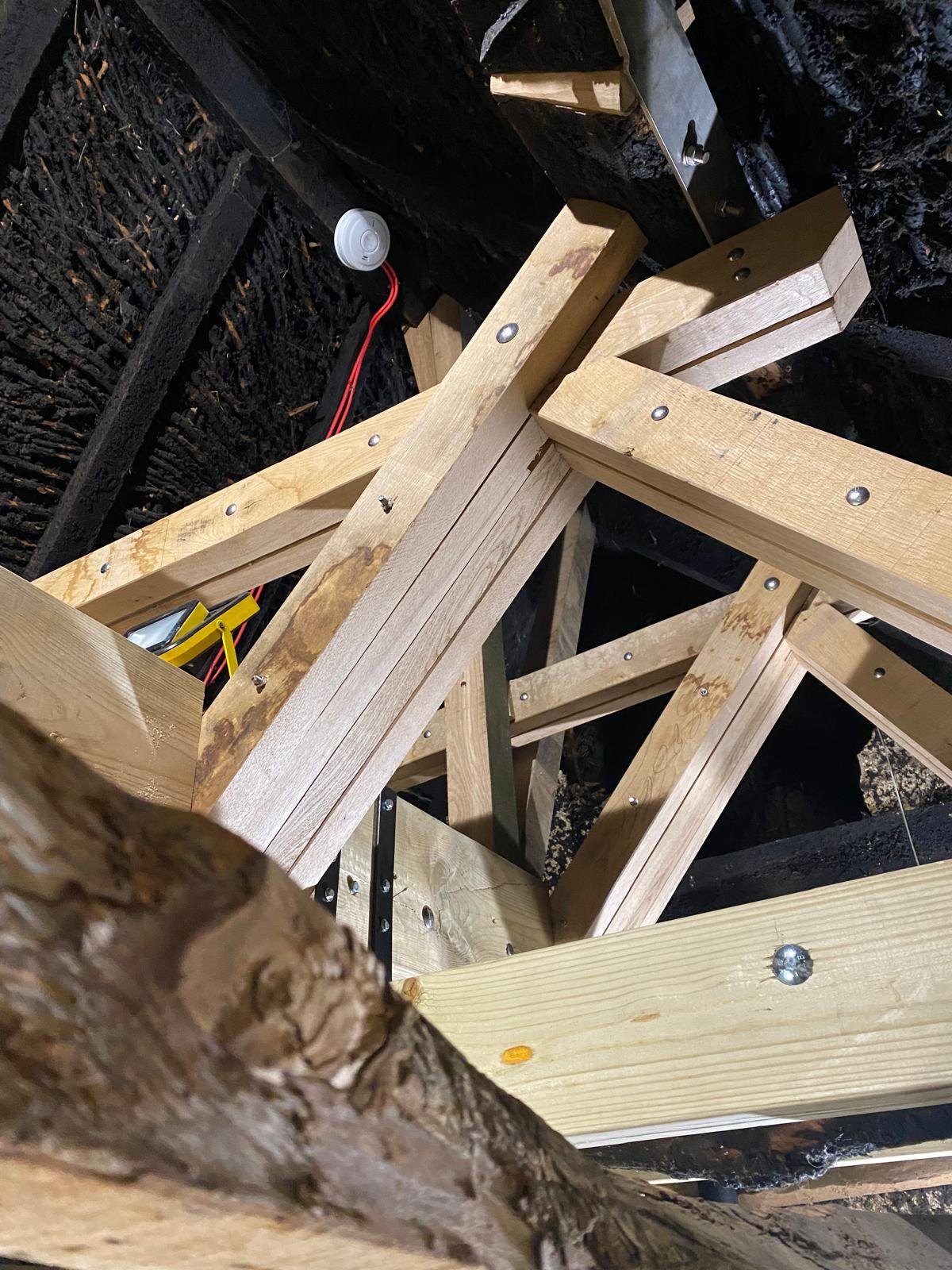 Wooden framing structure under construction with visible screws, black insulation, and wiring, in an indoor setting.