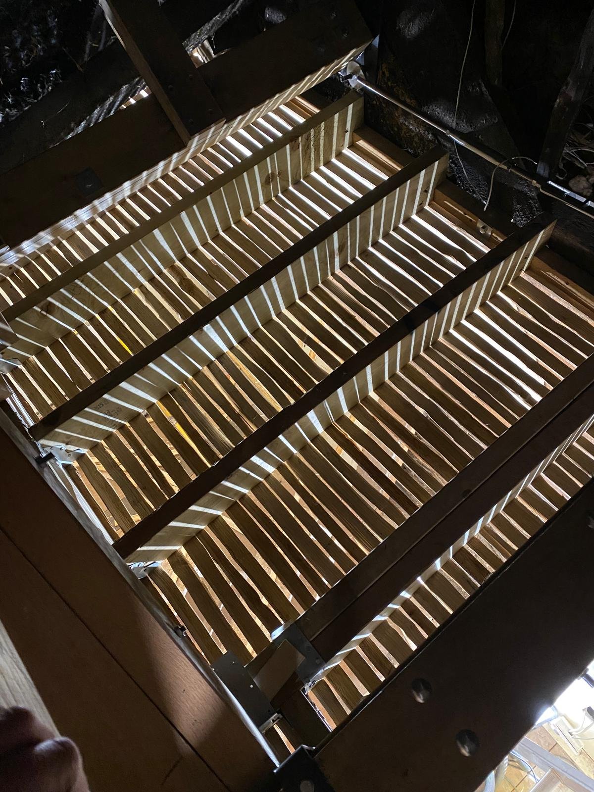 Wooden slatted structure, possibly a bed frame or a cage, with suspended wires and a dark background.