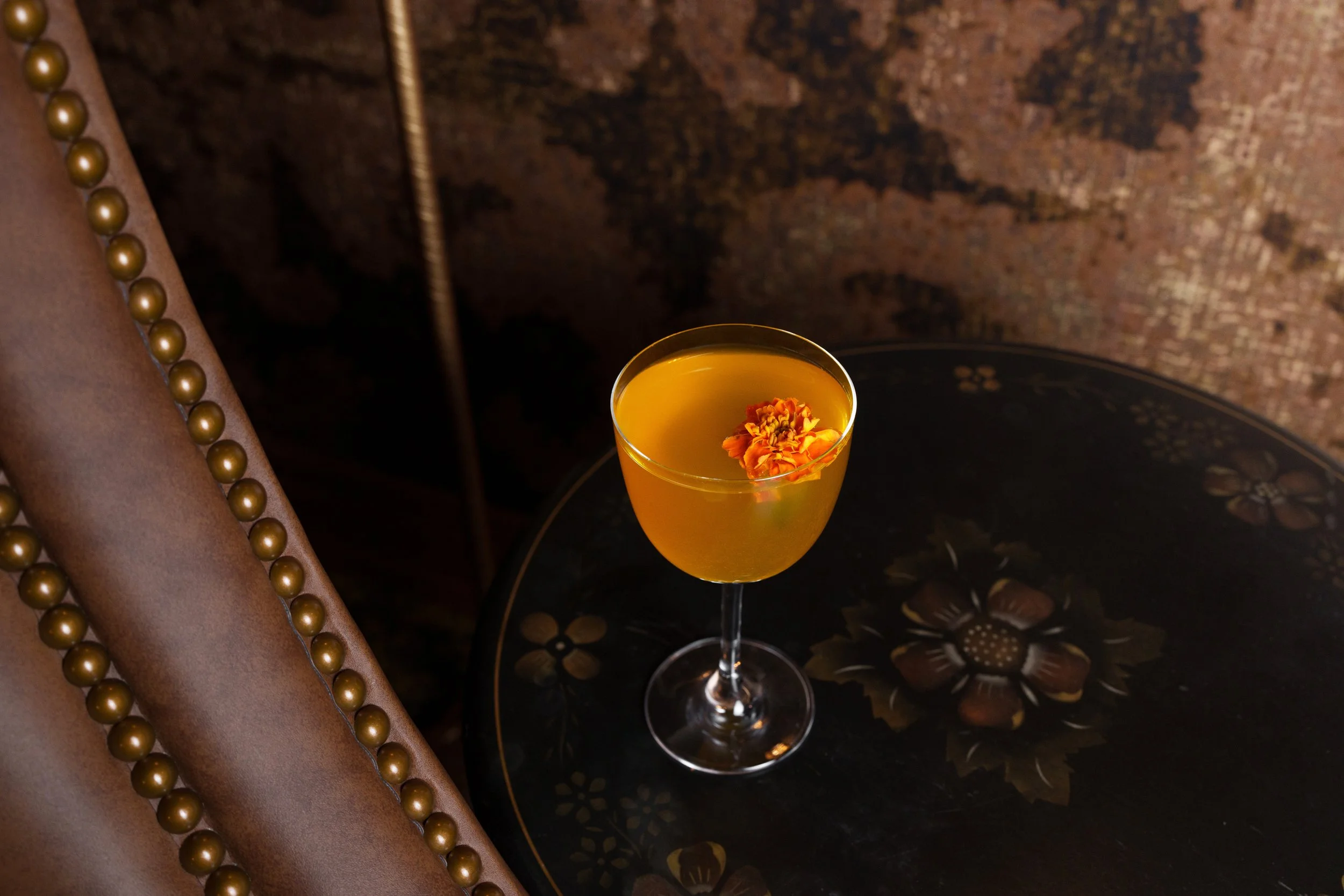 Yellow cocktail with an edible flower on a floral table.