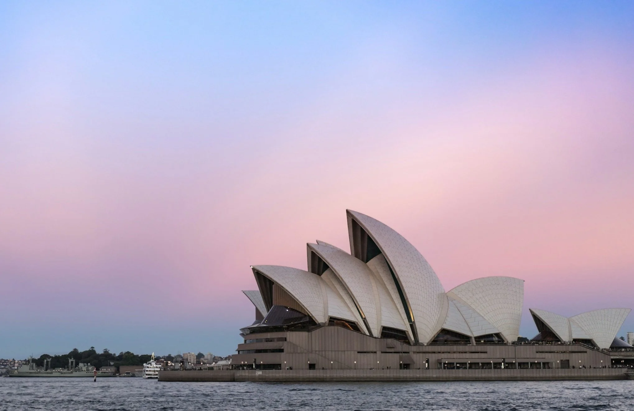 Sydney Opera House with a pink and blue sky in the background, viewed from the water.