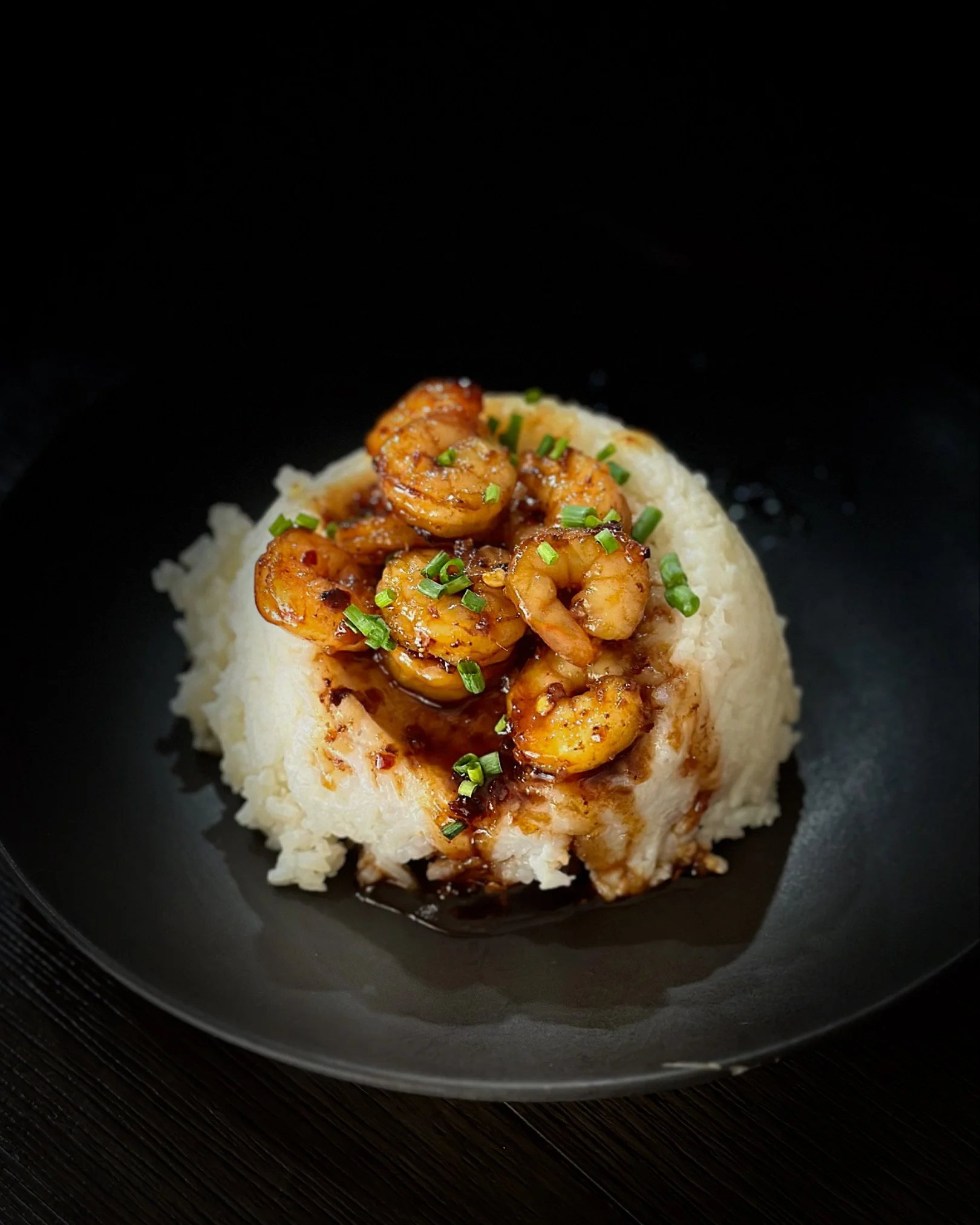 Shrimp served over mashed potatoes with green herbs and sauce on black plate.