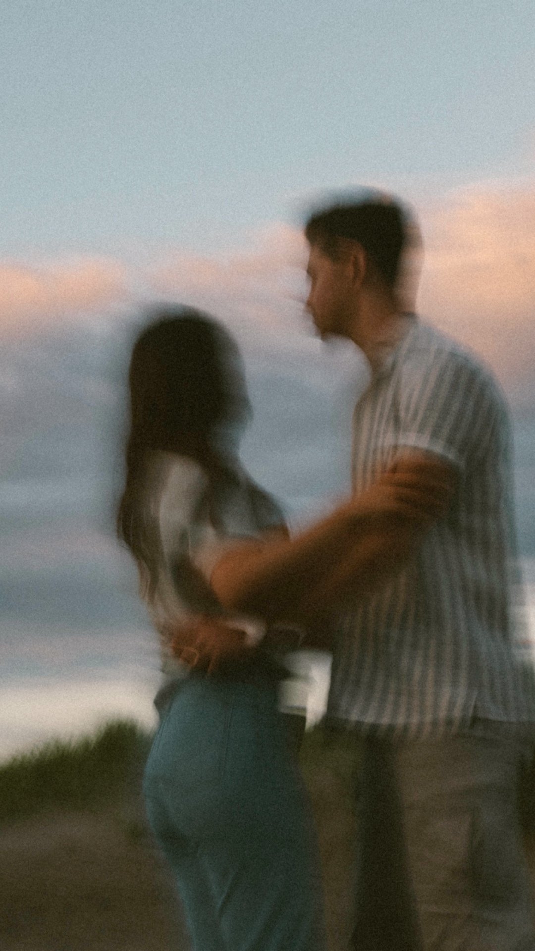 Blurry image of a couple embracing outdoors under a cloudy sky.