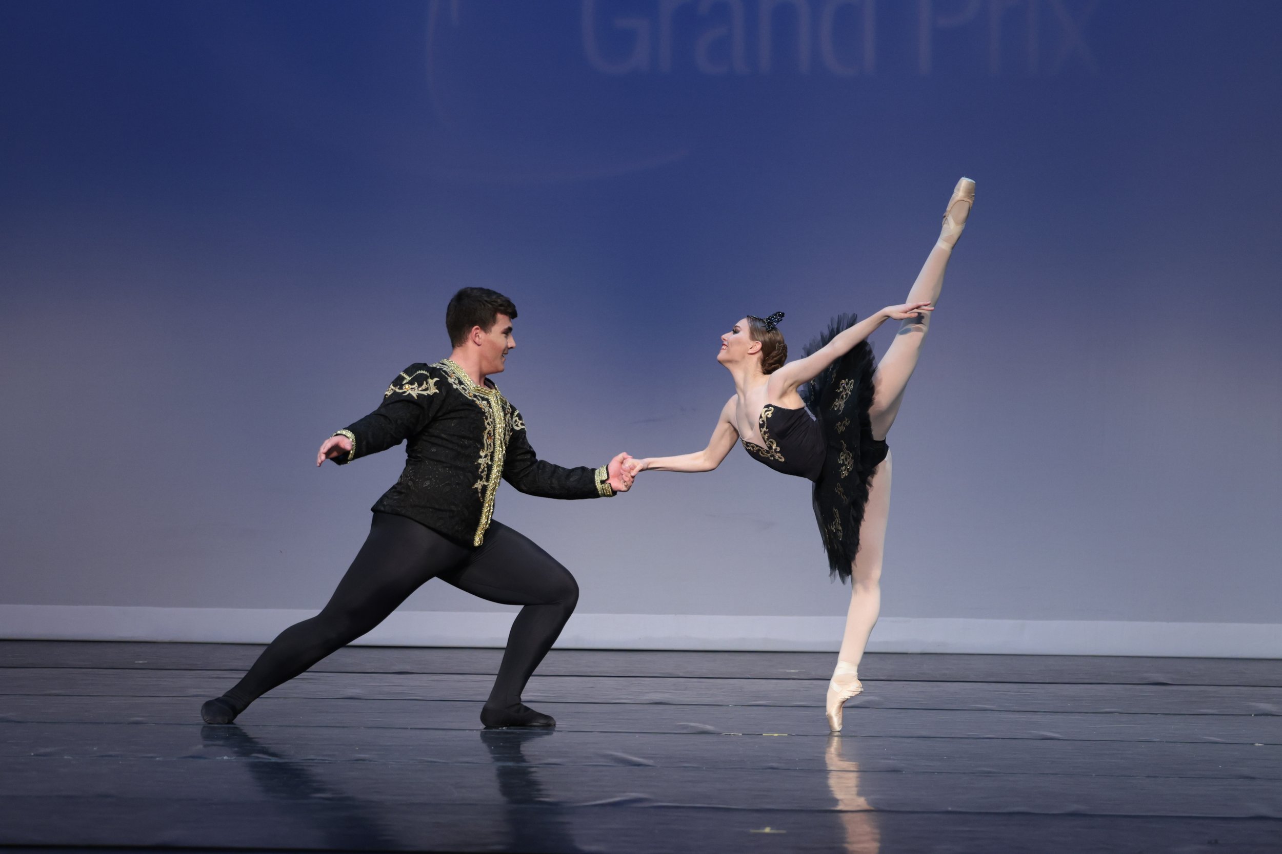 Sufian Khmous and a ballet dancer performing on stage, with a male dancer in a black costume supporting a female dancer in a black tutu executing an arabesque.