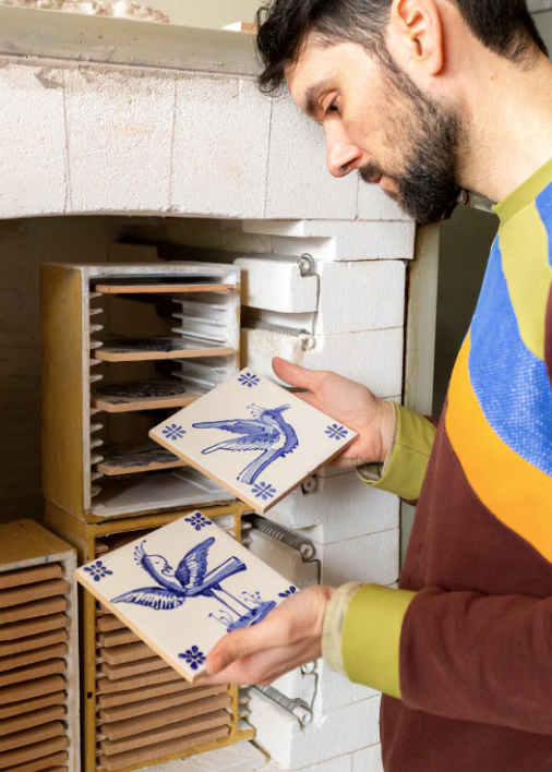A man examining decorative ceramic tiles with bird illustrations from a kiln or tile oven.