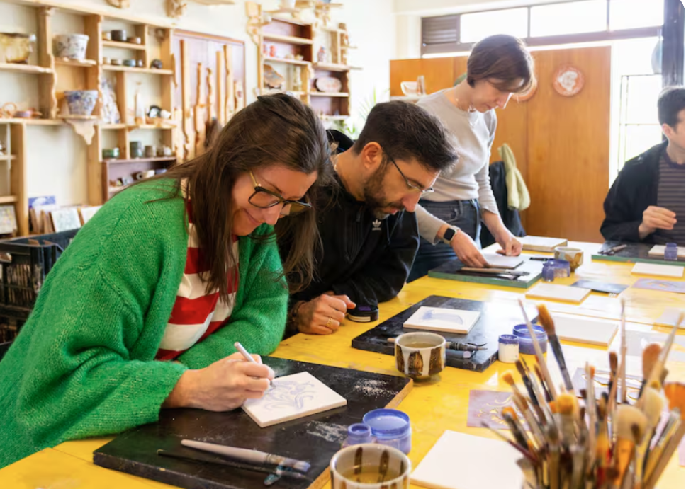 People working on ceramic art projects around a yellow table in an art studio.