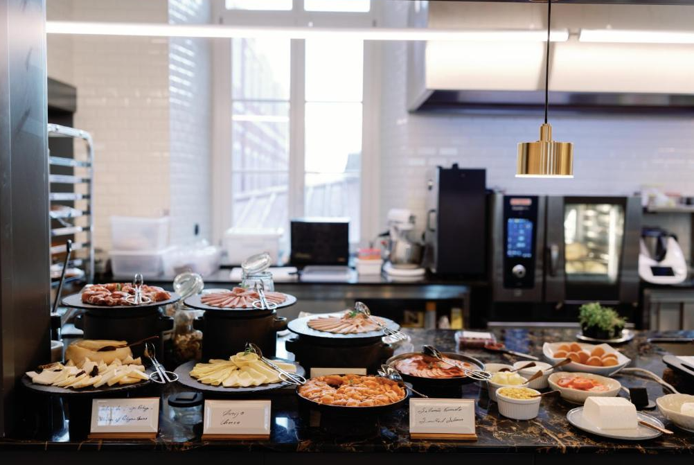 Buffet spread with assorted cheeses, sliced meats, eggs, and other breakfast items in a modern kitchen.