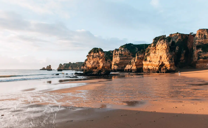 Beach with cliffs and rocks, gentle waves, and a person standing near the shoreline
