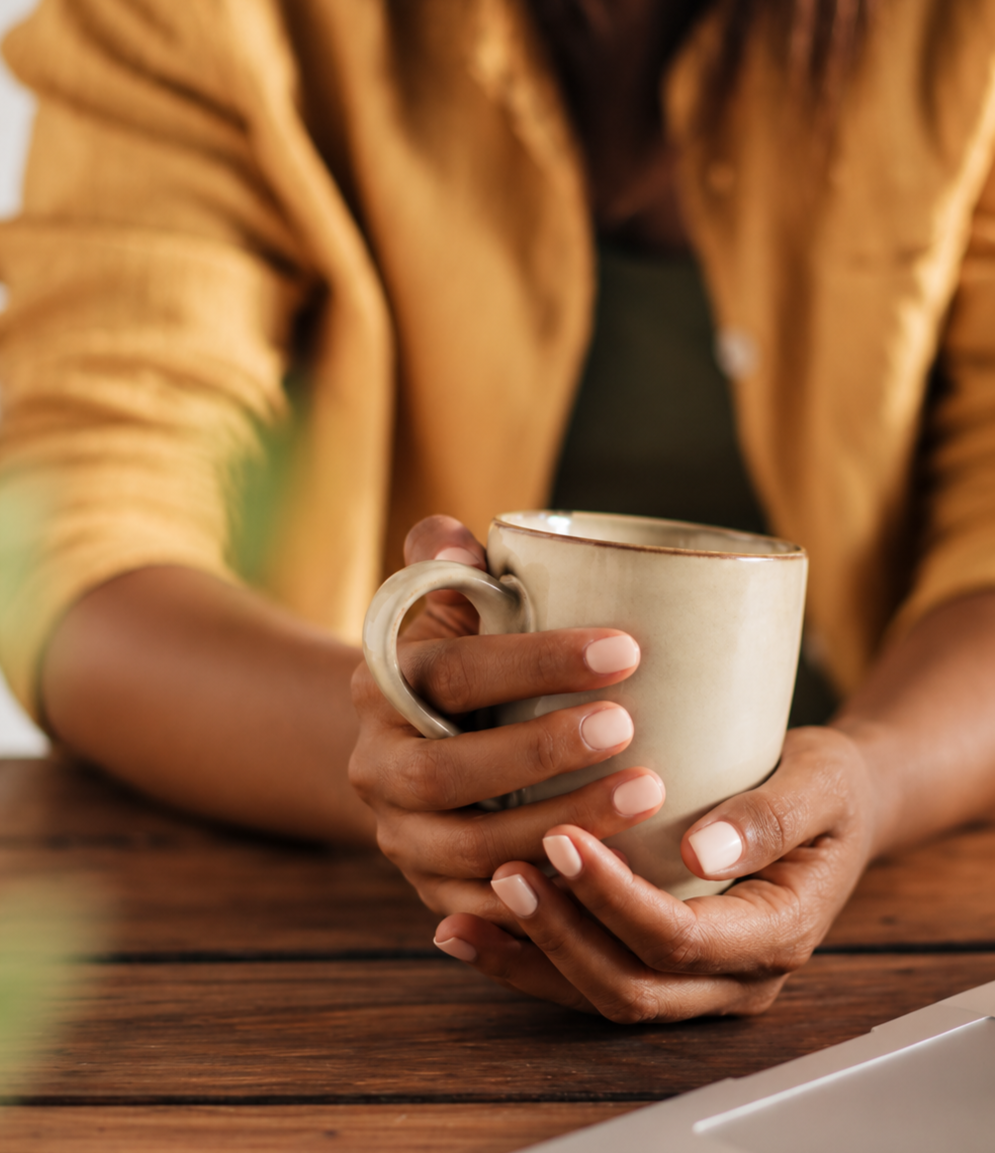 Person holding a cup of tea beside a laptop, illustrating the comfort of online therapy.