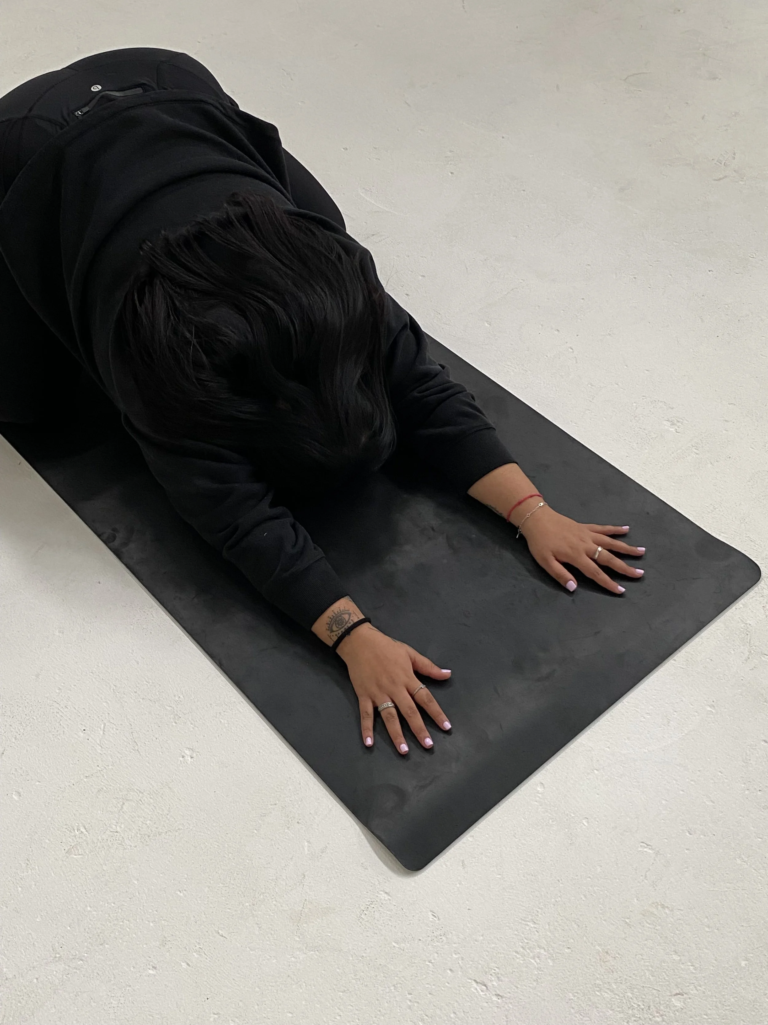 Prishaniee practicing yoga in child's pose on a black mat on a light-colored floor.