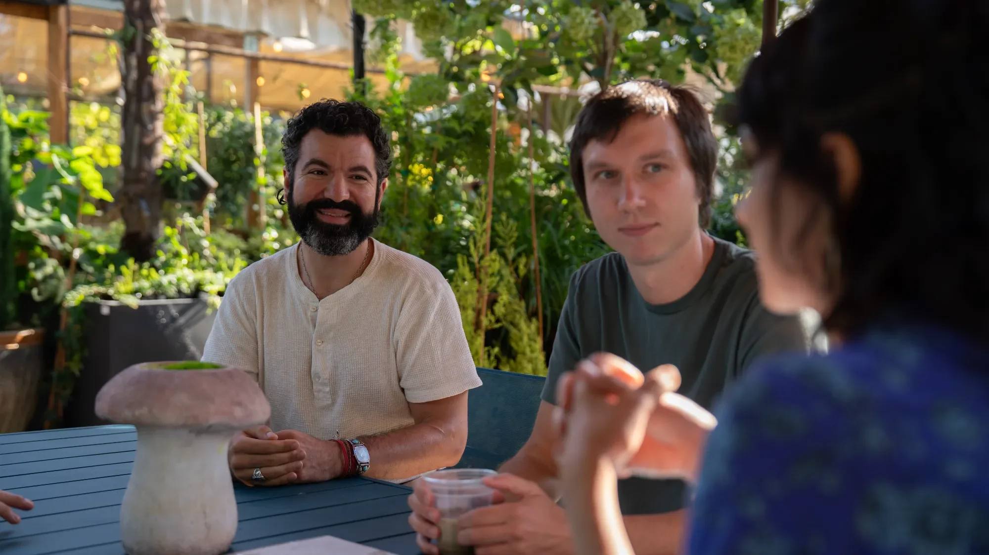 A woman and a man walking and talking outdoors on a dirt path surrounded by trees and bushes.