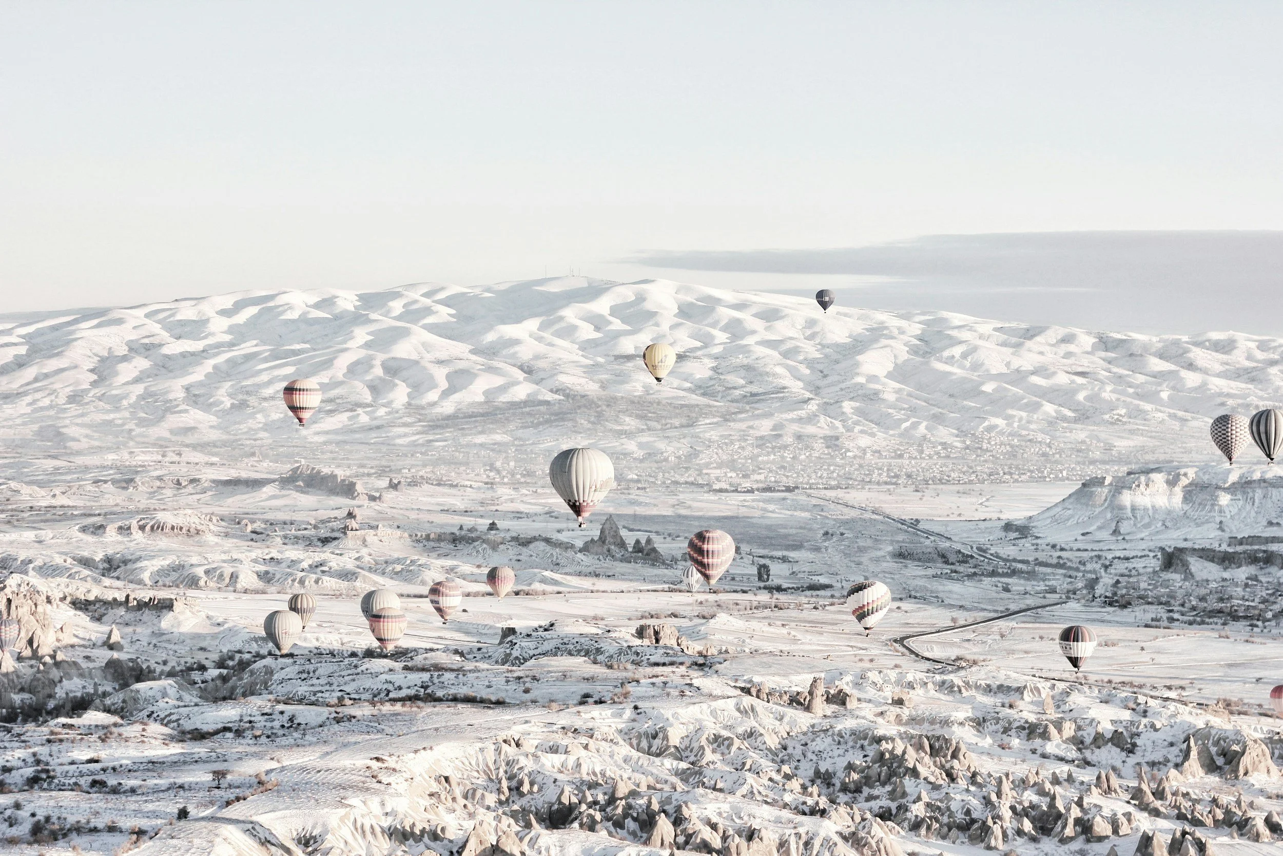 Multiple hot air balloons floating over a snow-covered landscape with mountains in the background.