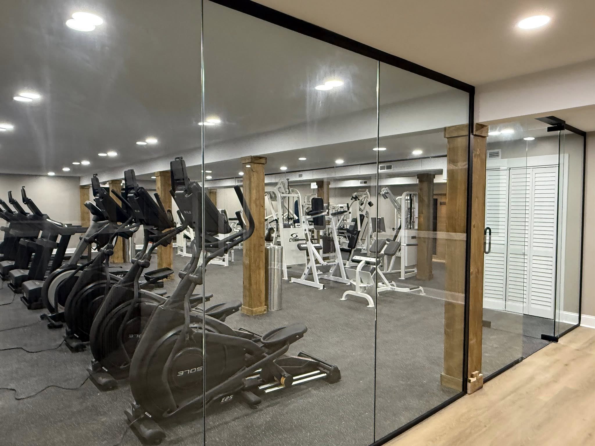 Glass-walled gym with cardio machines like elliptical trainers and a separate area with strength training equipment.