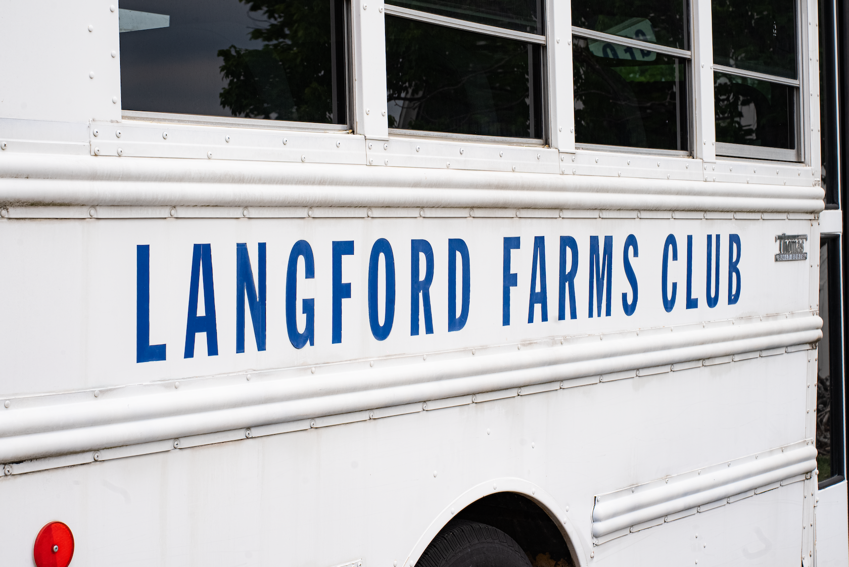 Side view of a white vehicle or trailer with blue text that reads 'LANGFORD FARMS CLUB' and small windows.