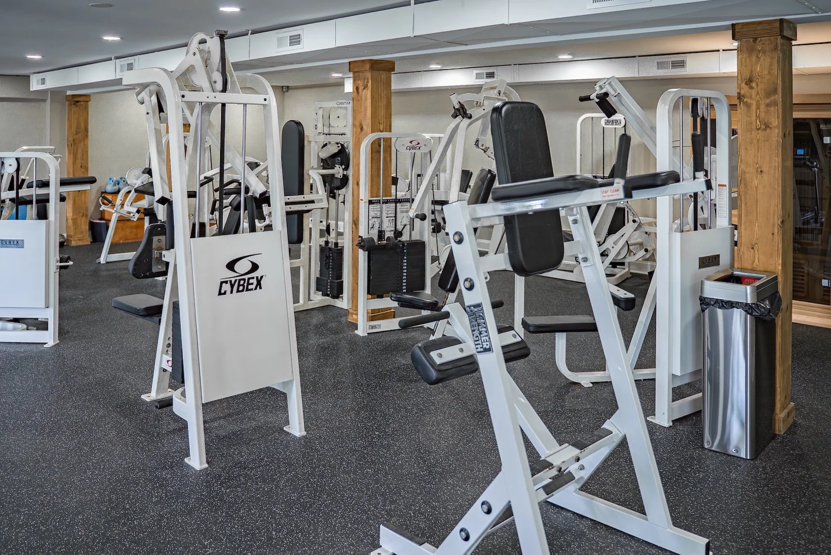 Exercise equipment in a gym, including weight machines and a trash can.