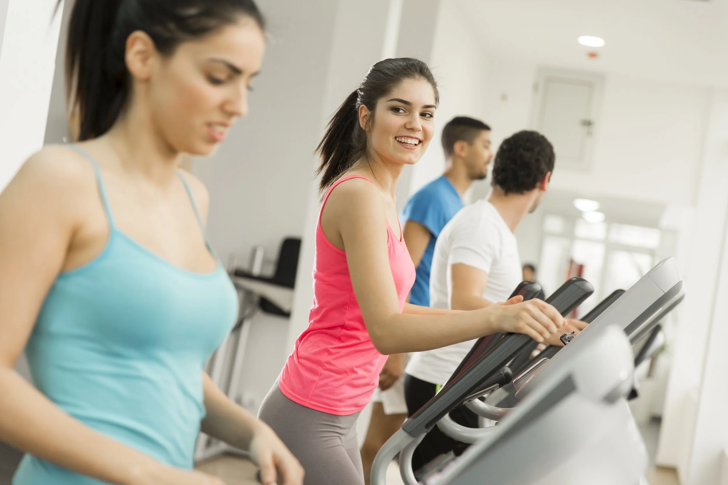 A group of people using treadmills at a gym, with a woman smiling and looking at the camera.