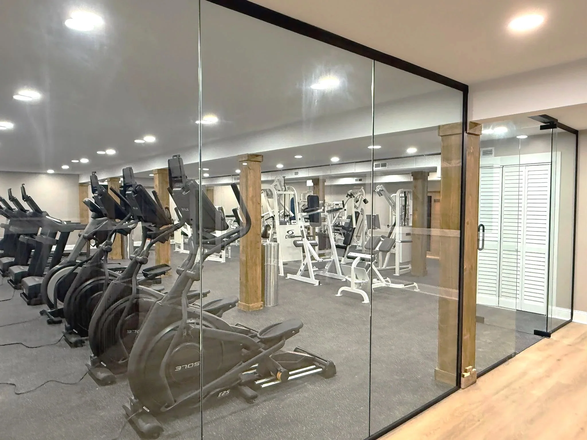 Fitness center with elliptical trainers and weight machines seen through glass wall.