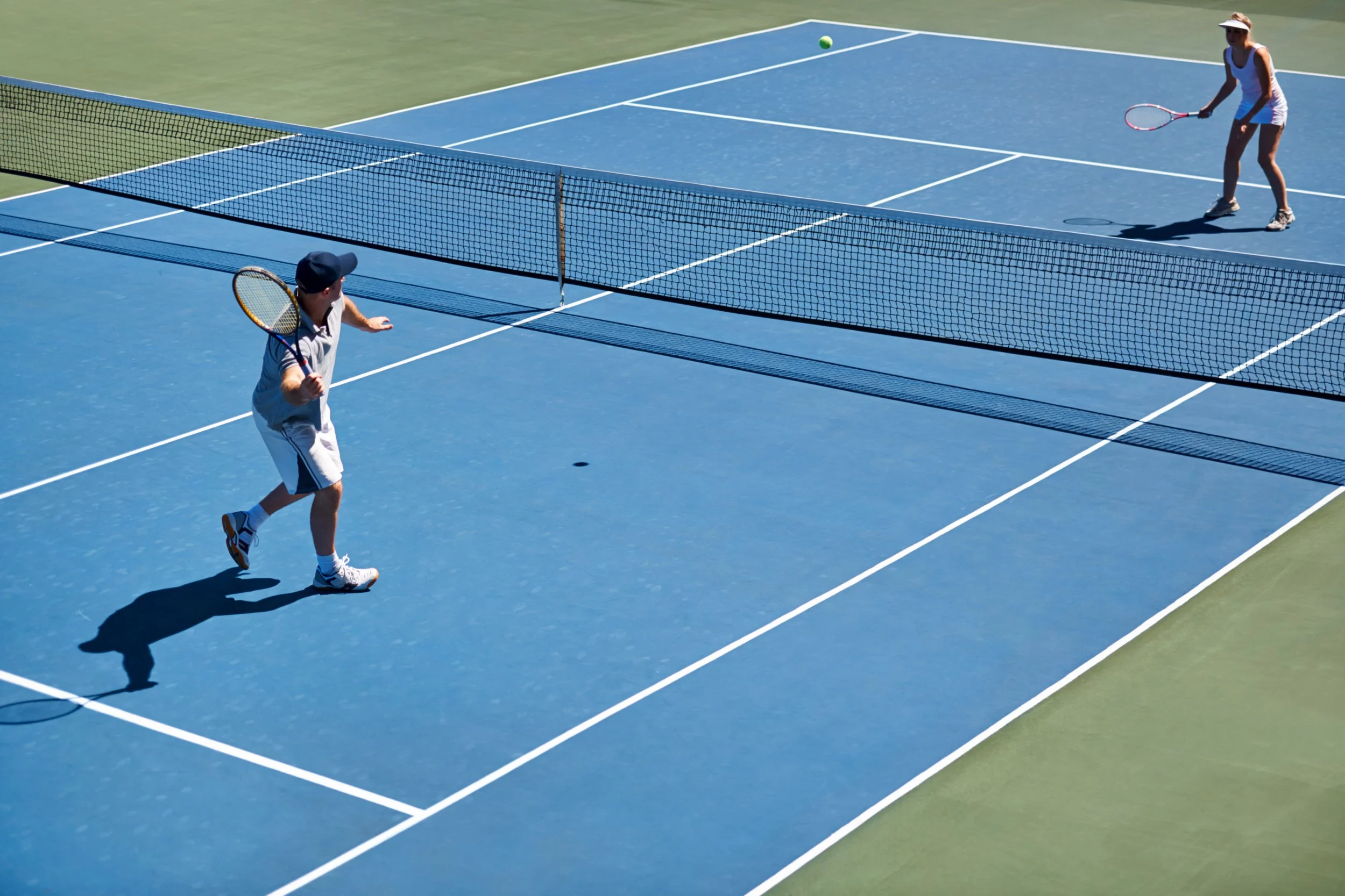 Two people playing pickleball on a blue court with a net, with one person hitting the ball and the other preparing to hit.