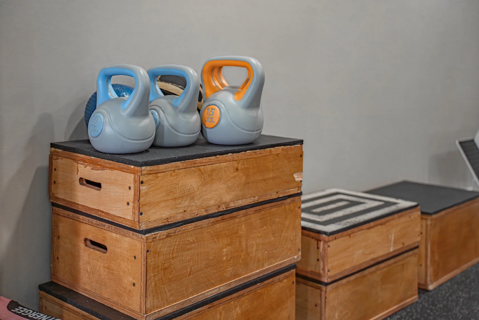 Four kettlebells with weights labeled 10 and 15 lbs on top of wooden exercise boxes in a gym.