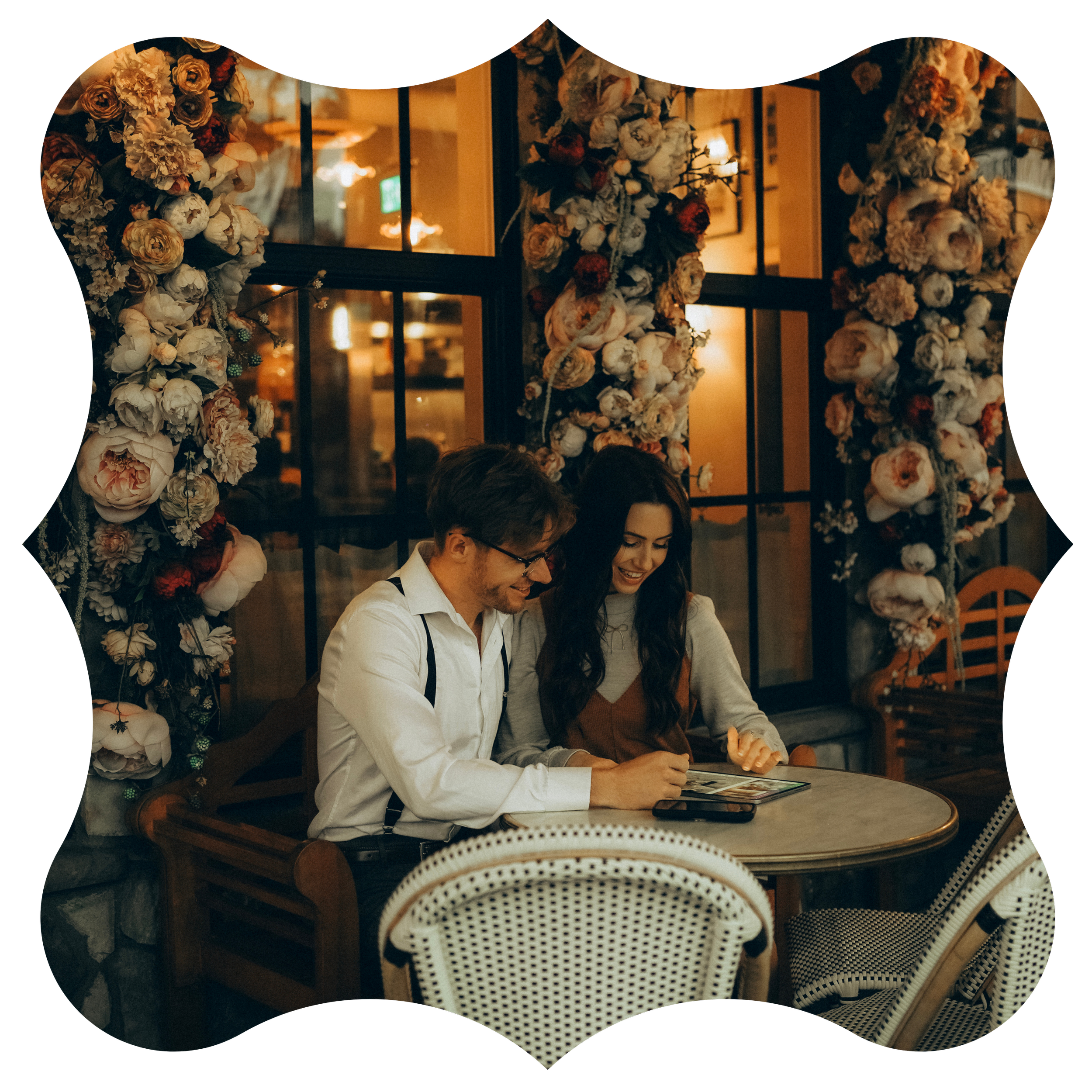 A man and a woman sitting at a table in a warmly lit restaurant with floral wall decorations, looking at a menu and smiling.