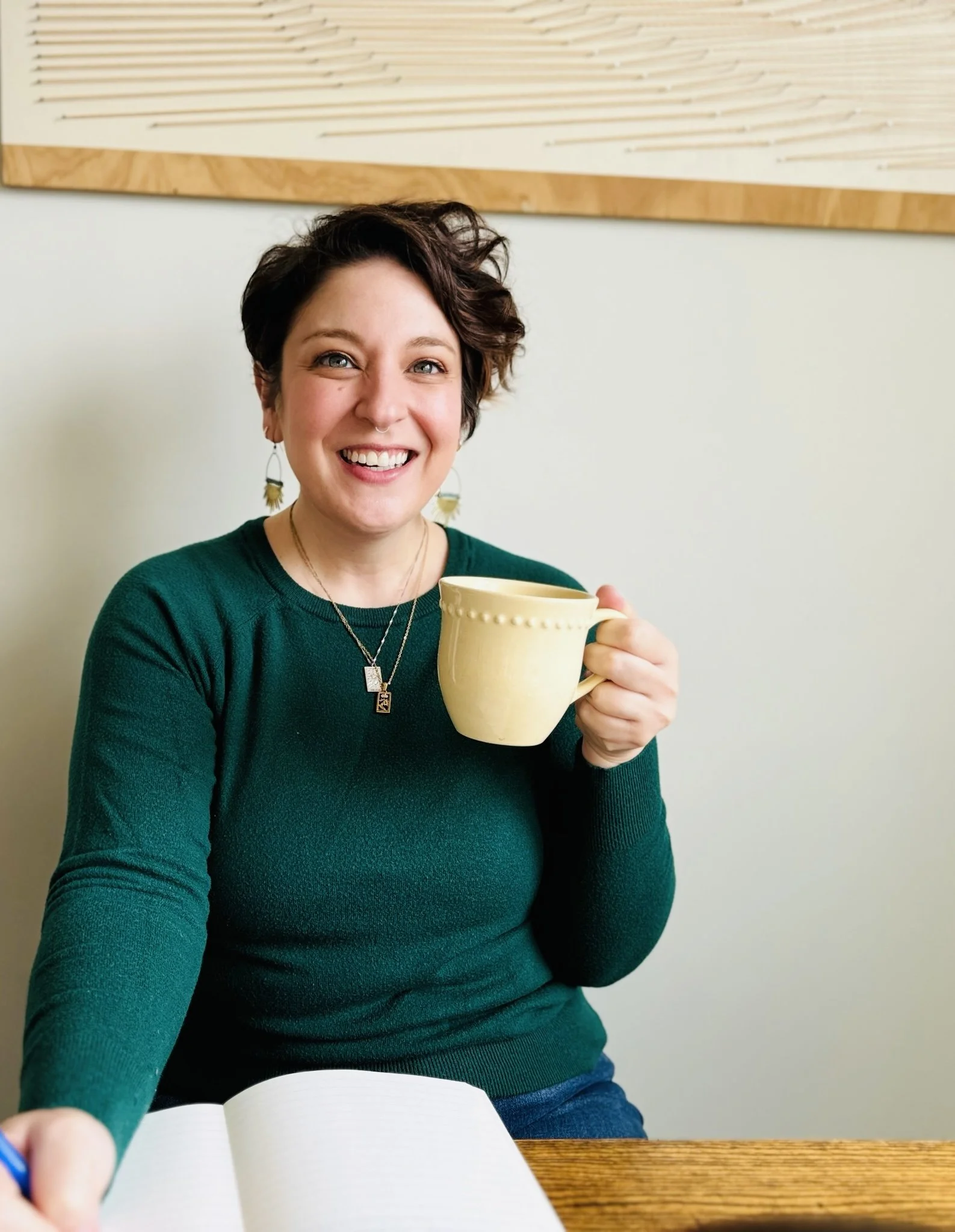 Image of Rae holding a yellow mug of coffee in one hand and a pen in a notebook in the other hand.