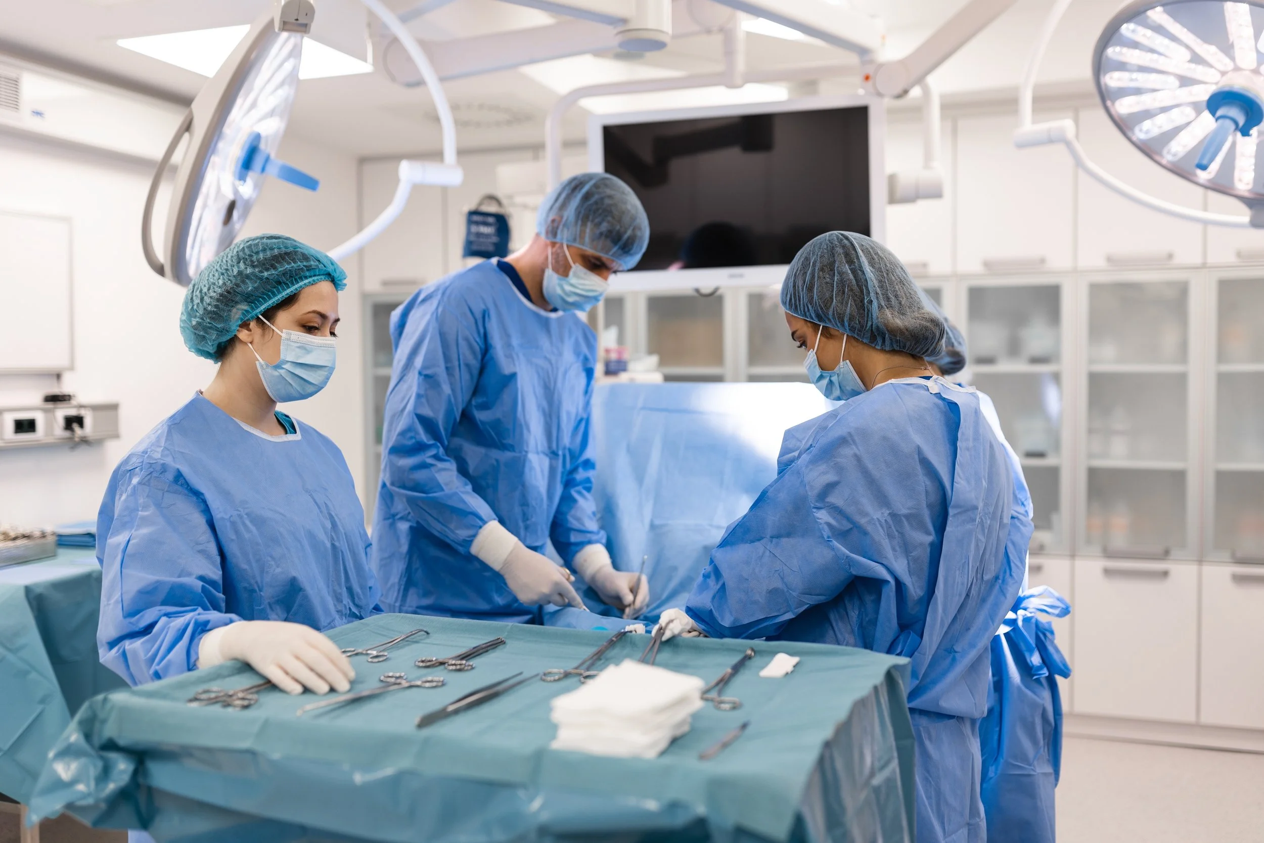 Medical team in surgical gowns, masks, and gloves performing surgery in an operating room with surgical instruments on a sterile drape