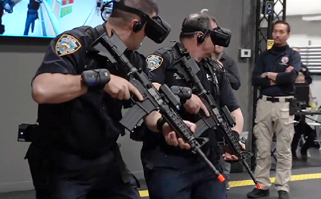 Three police officers wearing virtual reality headsets holding rifles during a demonstration or training session in an indoor facility, with a man observing in the background.