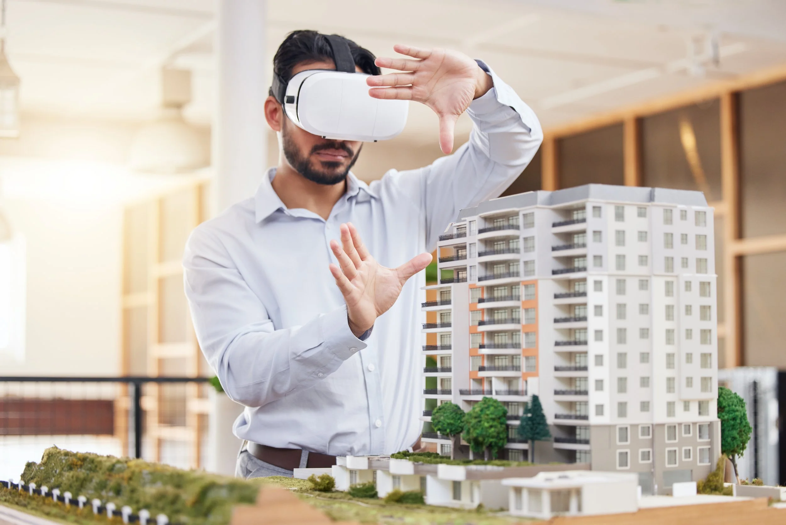 A man wearing a white shirt and virtual reality headset exploring a detailed architectural model of a modern apartment building.