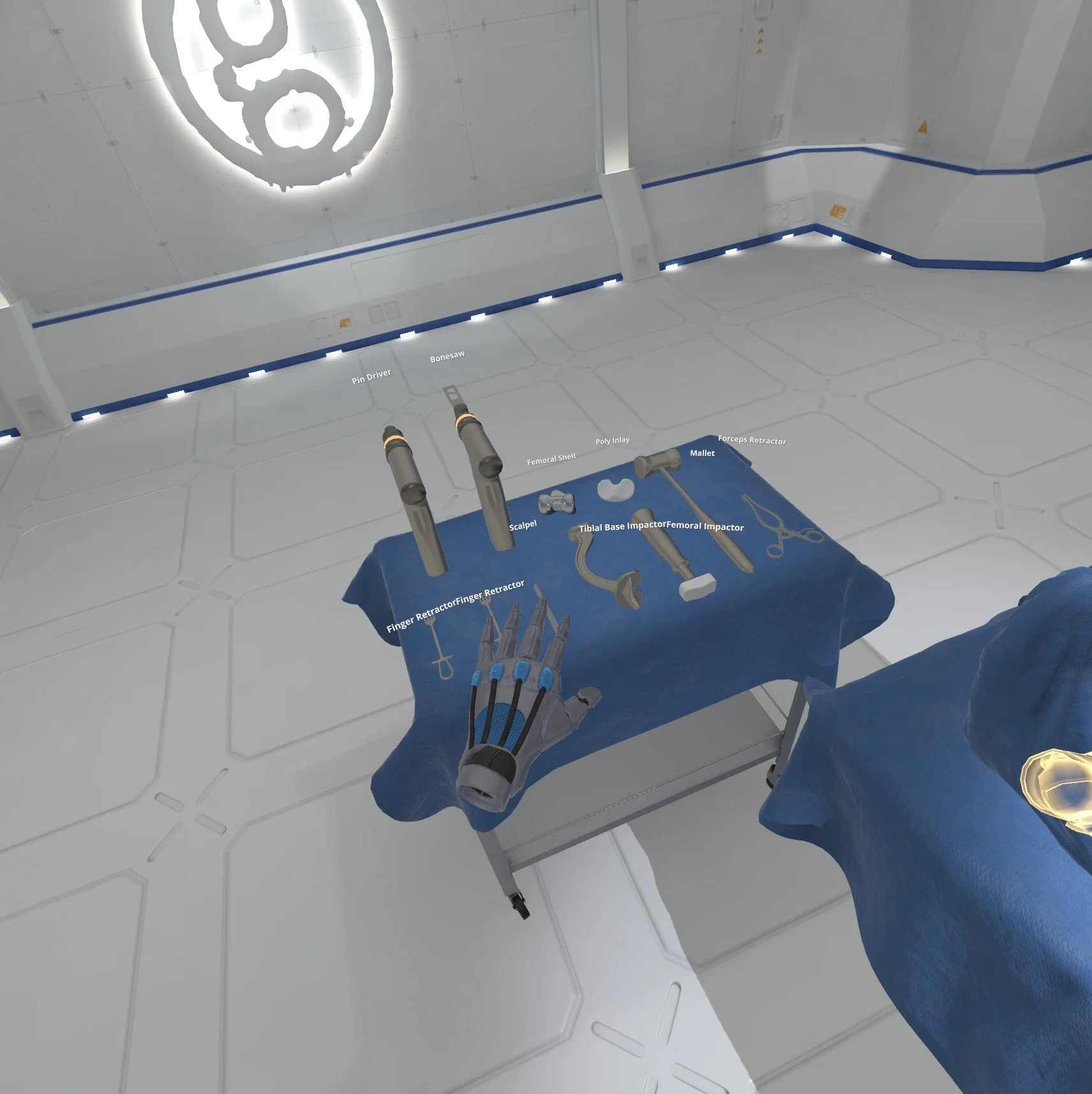 A virtual reality simulation of a surgical setup with various labeled orthopedic tools on a blue cloth, including pin driver, bone saw, scalpel, mallet, forceps retractor, tibial base impactor, femoral impactor, finger retractor, and femoral shell, i