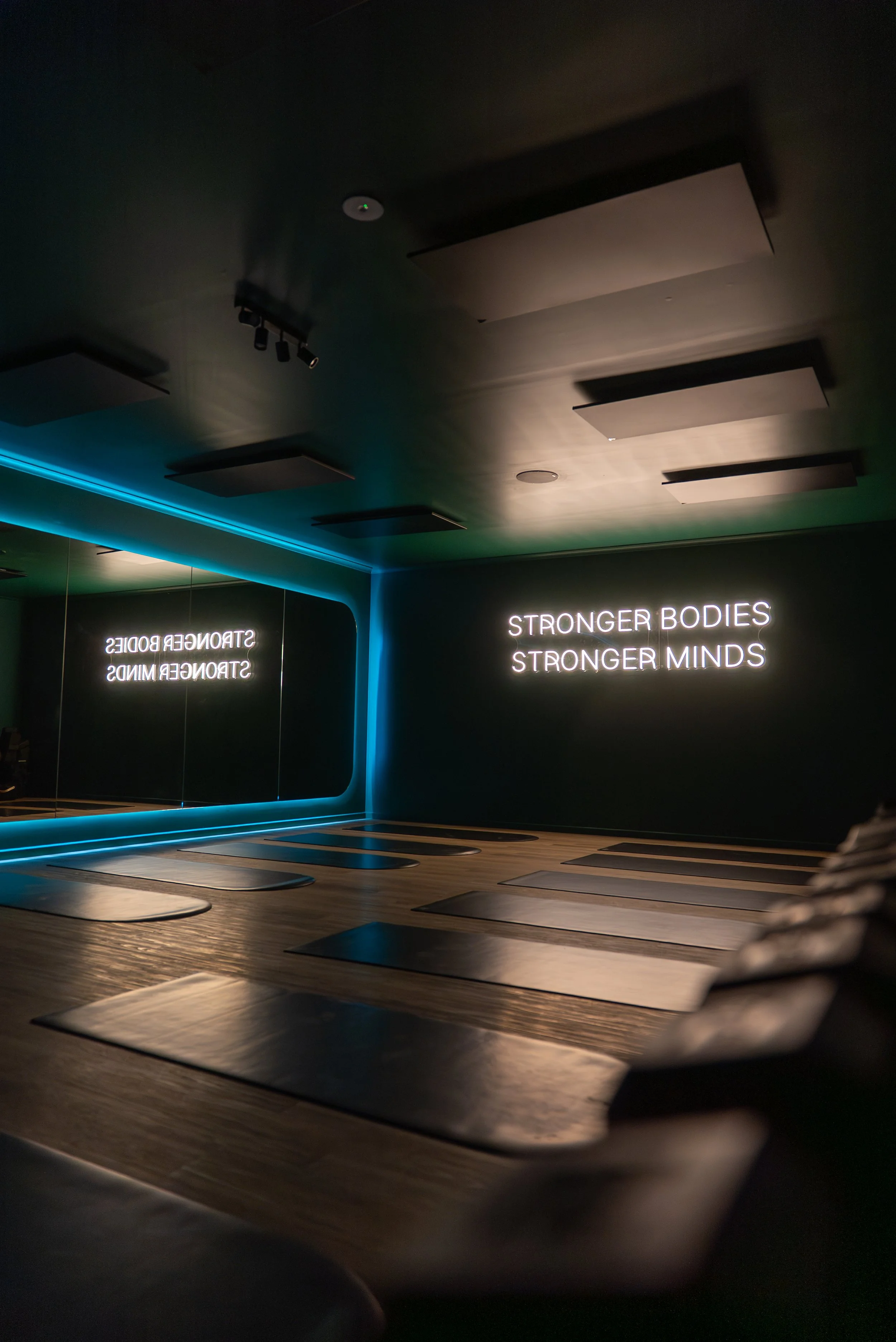 Person performing a pilates movement against a gray wall, wearing black leggings and an orange top.