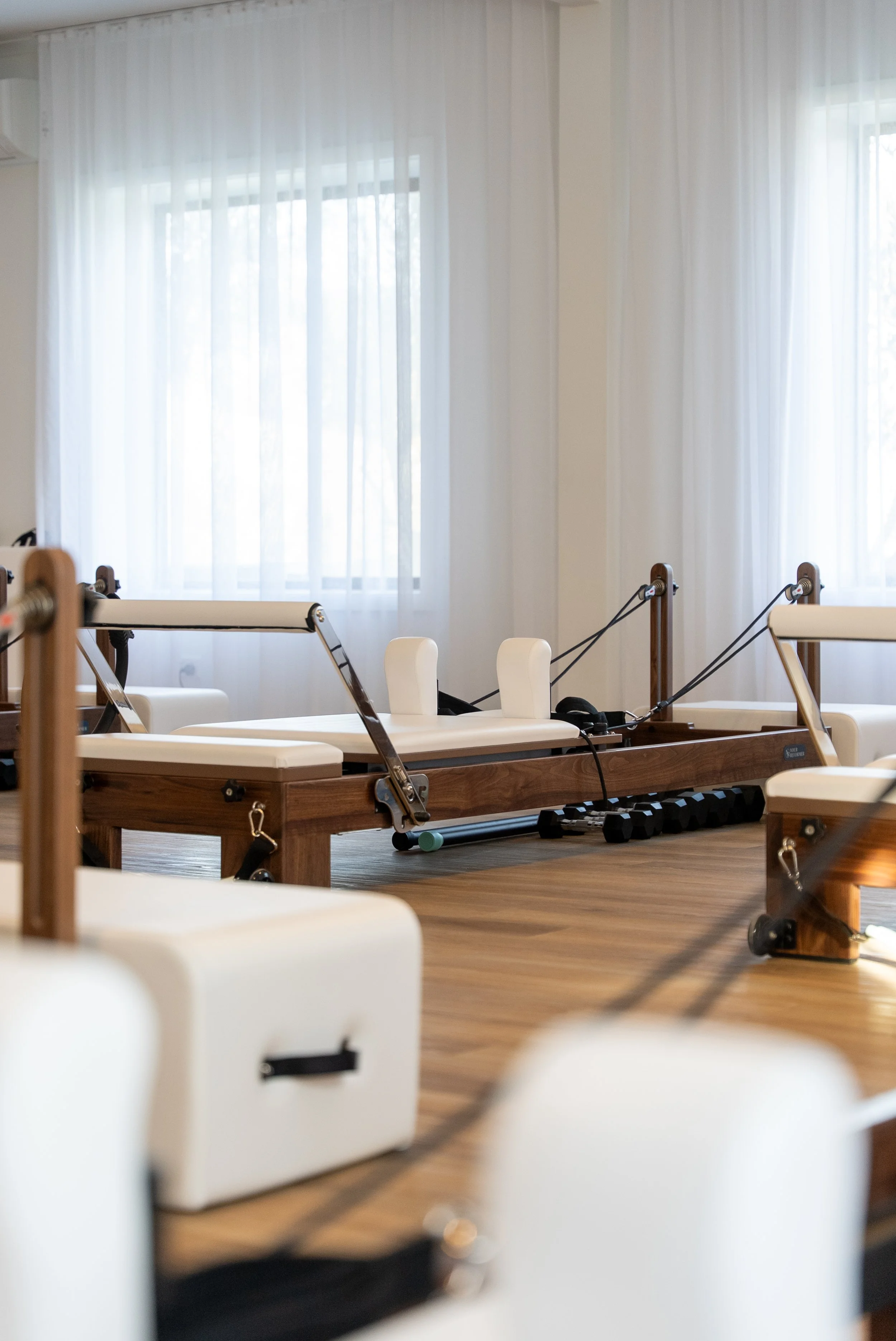 Pilates reformer machines lined up in a fitness studio with wooden frames and black padding.