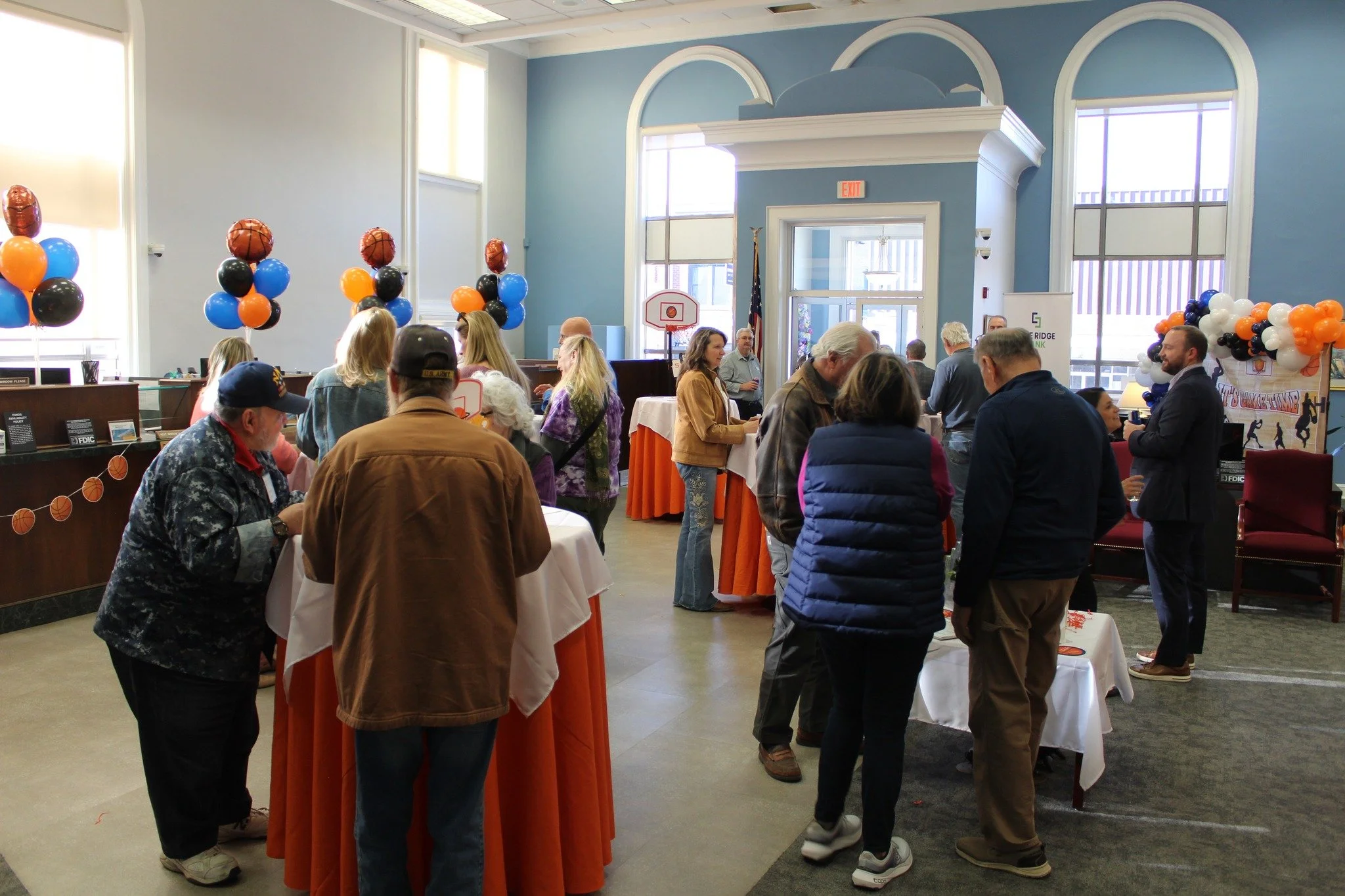 People mingling at an indoor event with balloons and tables.