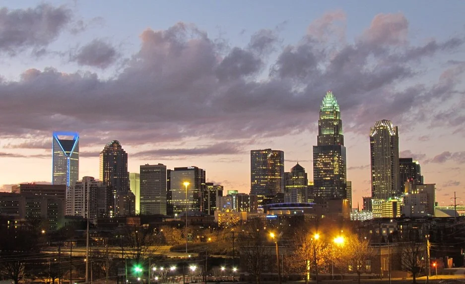 Charlotte skyline at dusk with lit buildings and colorful sky.
