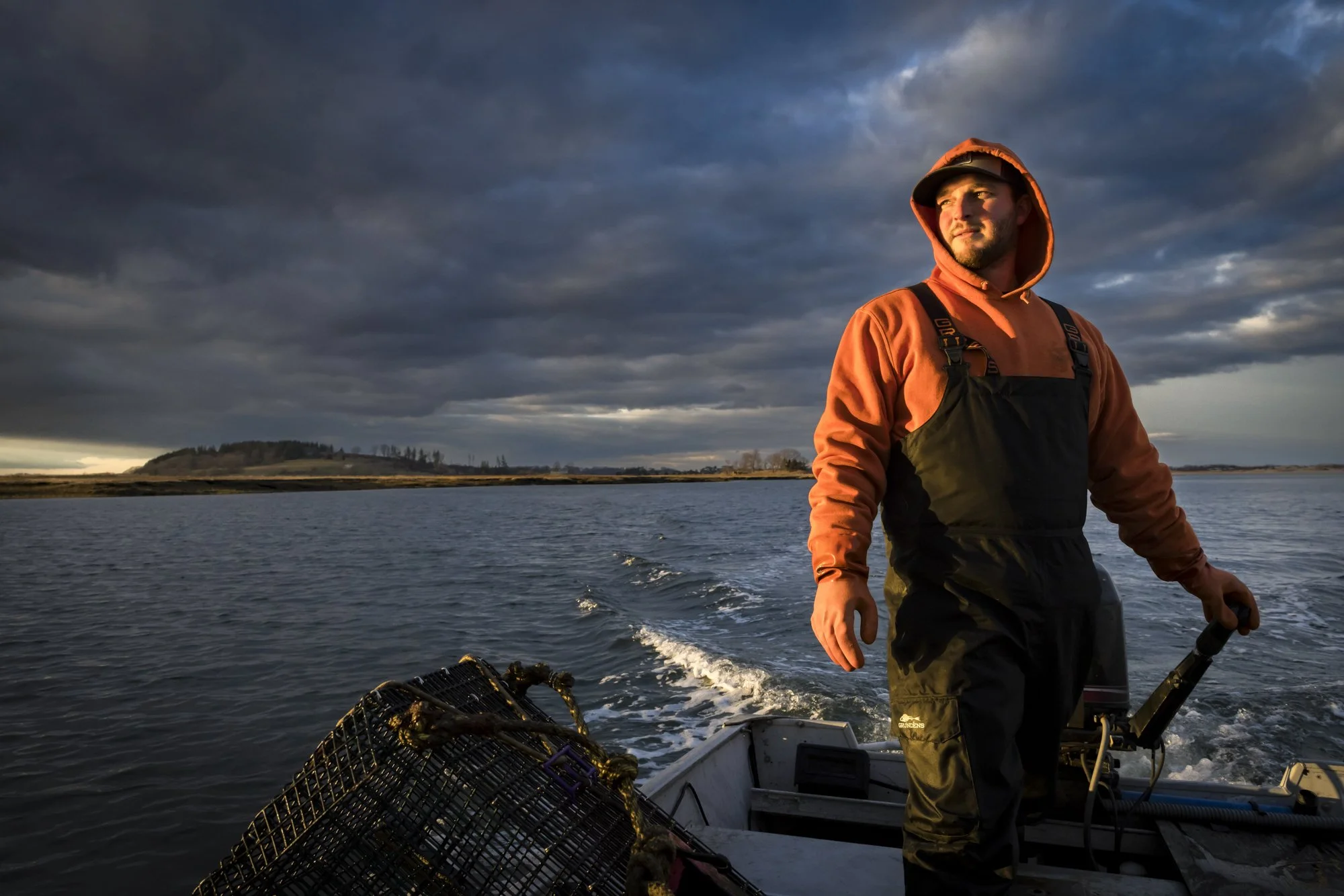 A green crab fisherman steers his skiff through the marshes of Gloucester, MA at golden hour. Considered an invasive threat, green crabs are now being harvested commercially for bait, culinary use, and innovative products like crab-based fertilizer a