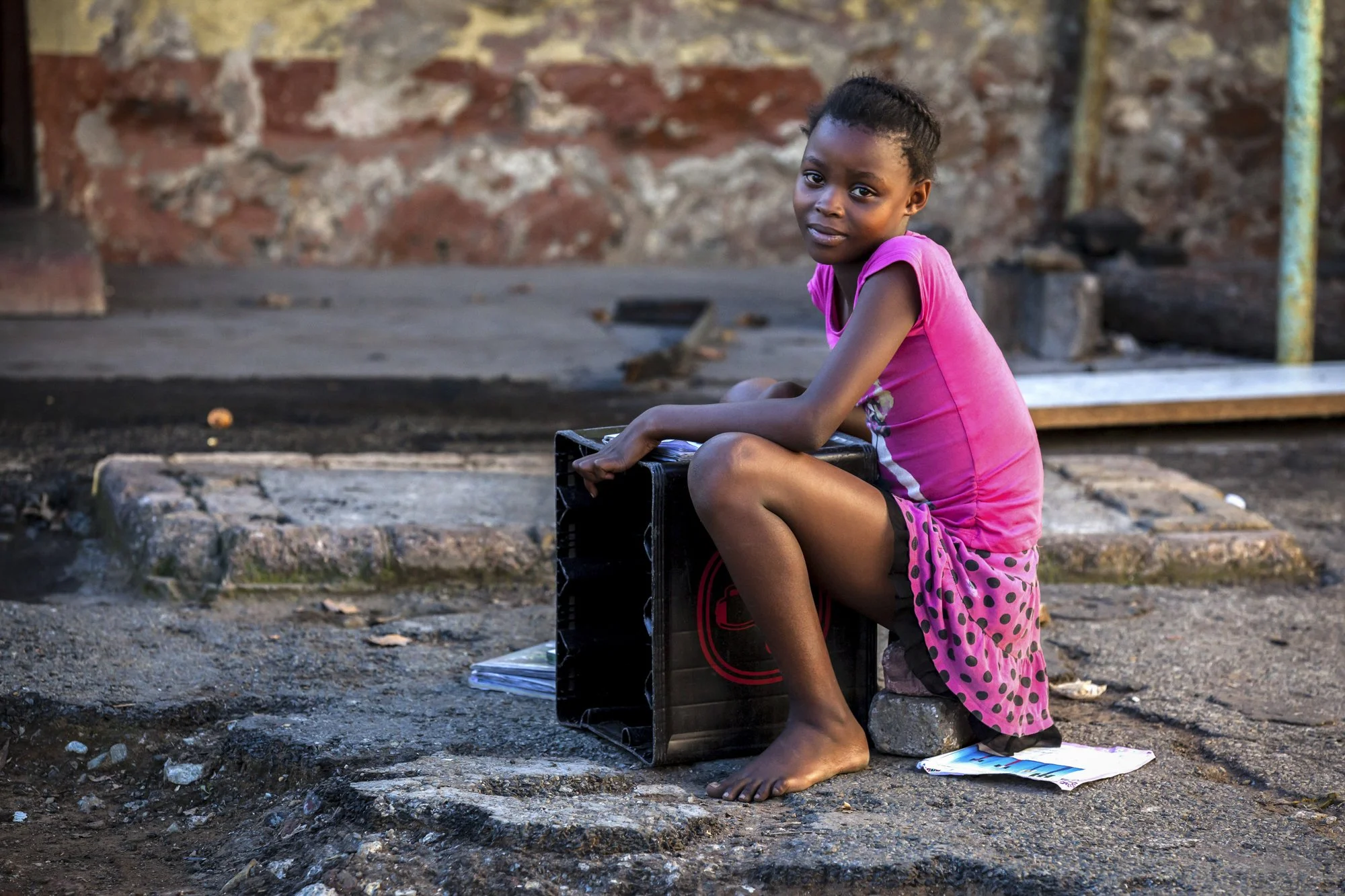 A young girl does her homework in the shadow of the abandoned Durban Deep mine, using a sideways crate as a makeshift desk and a pair of concrete blocks as her chair. For the migrant families now squatting in these derelict buildings, basic resources