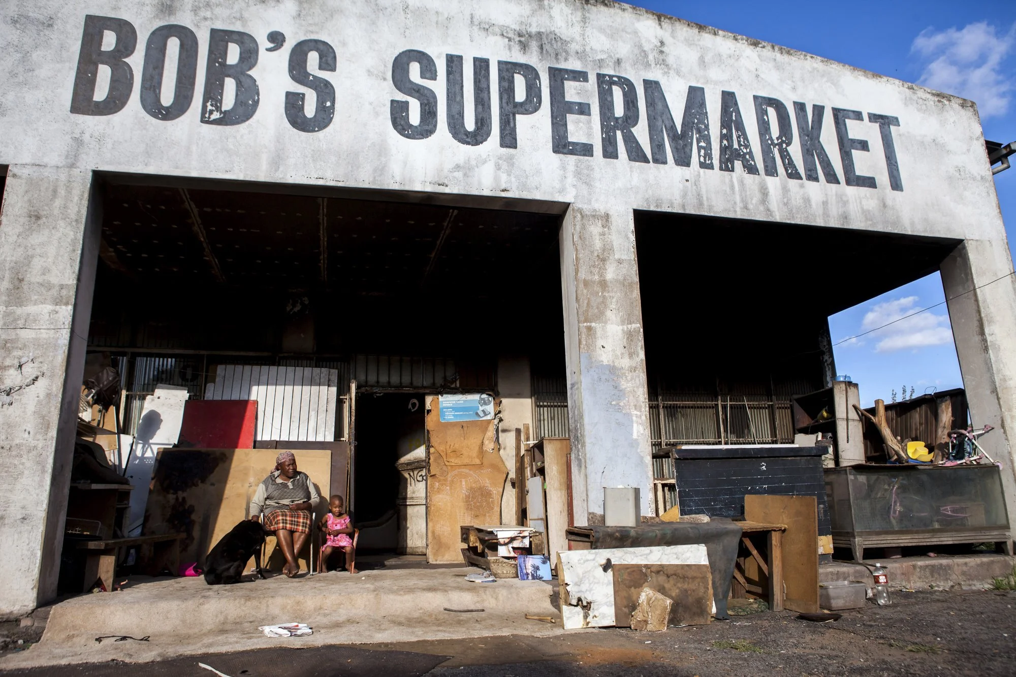 Once the bustling supermarket that served Durban Deep’s mining community, “Bob’s Supermarket” now shelters families who have carved makeshift rooms into its concrete shell. With no formal housing available, migrants and displaced South Africans have 