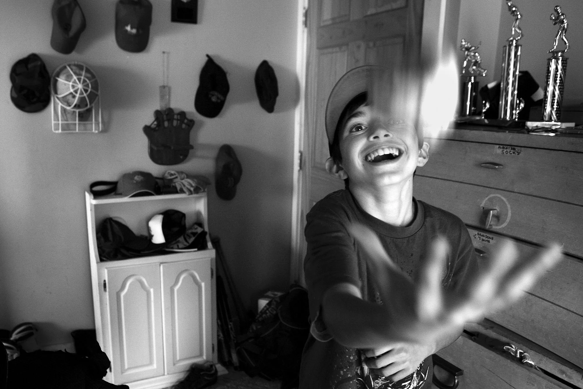 A boy plays with a baseball in his room in Peabody, Massachusetts, captured in a candid moment of joy and movement.
