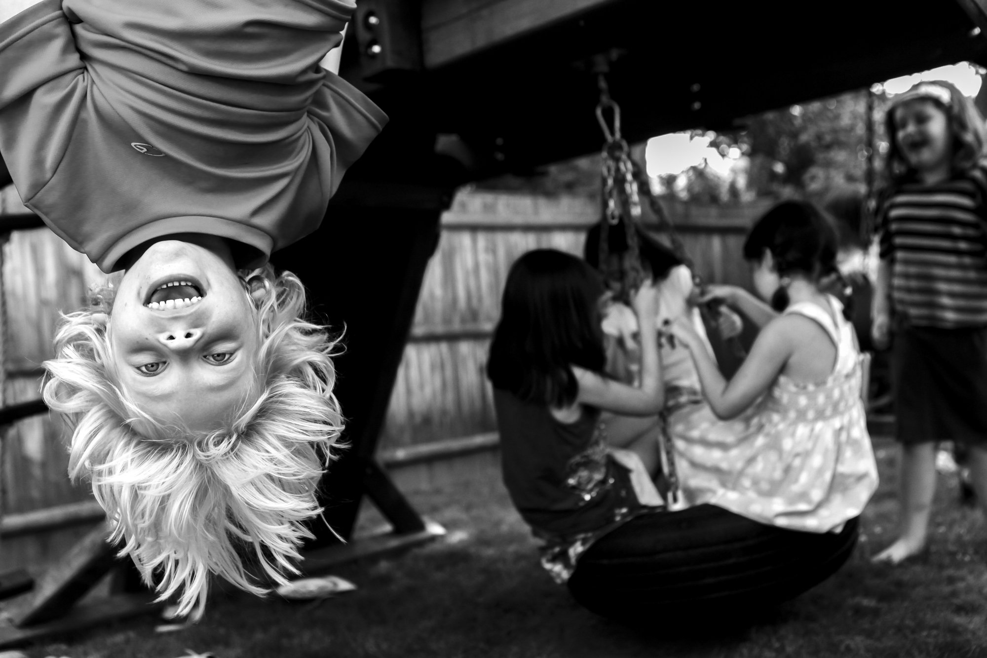 A child hangs upside down and laughs at a friend’s birthday party, capturing a spontaneous moment of childhood joy.